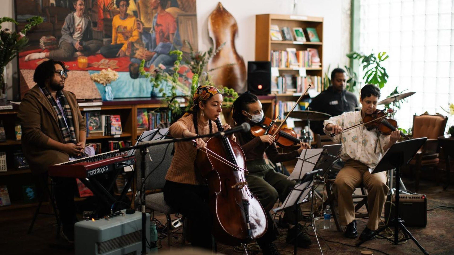 Musicians are shown on a stage surrounded by books and art