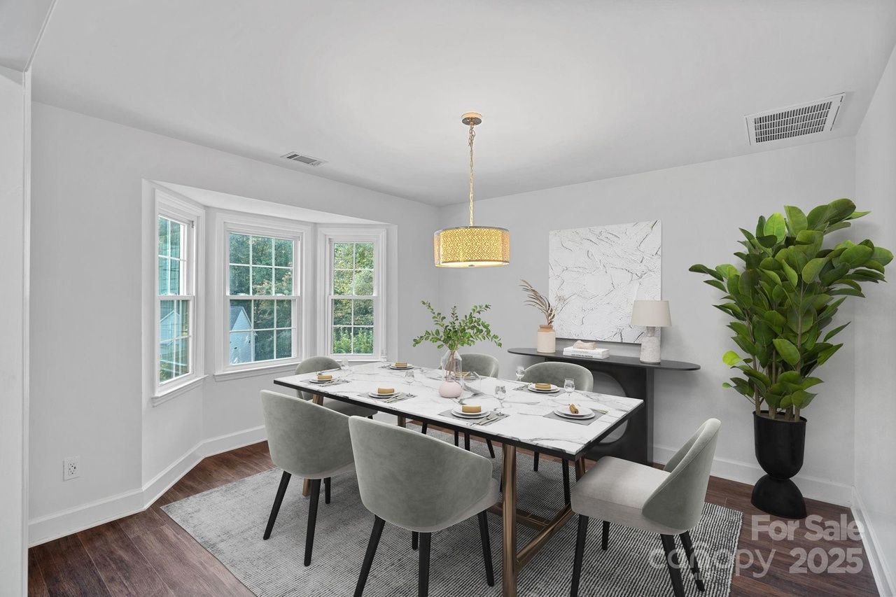 Bright dining room with white walls, a marble table set for six, light gray chairs, a large green plant in a black pot, a modern light fixture, and a console with decor under abstract art.