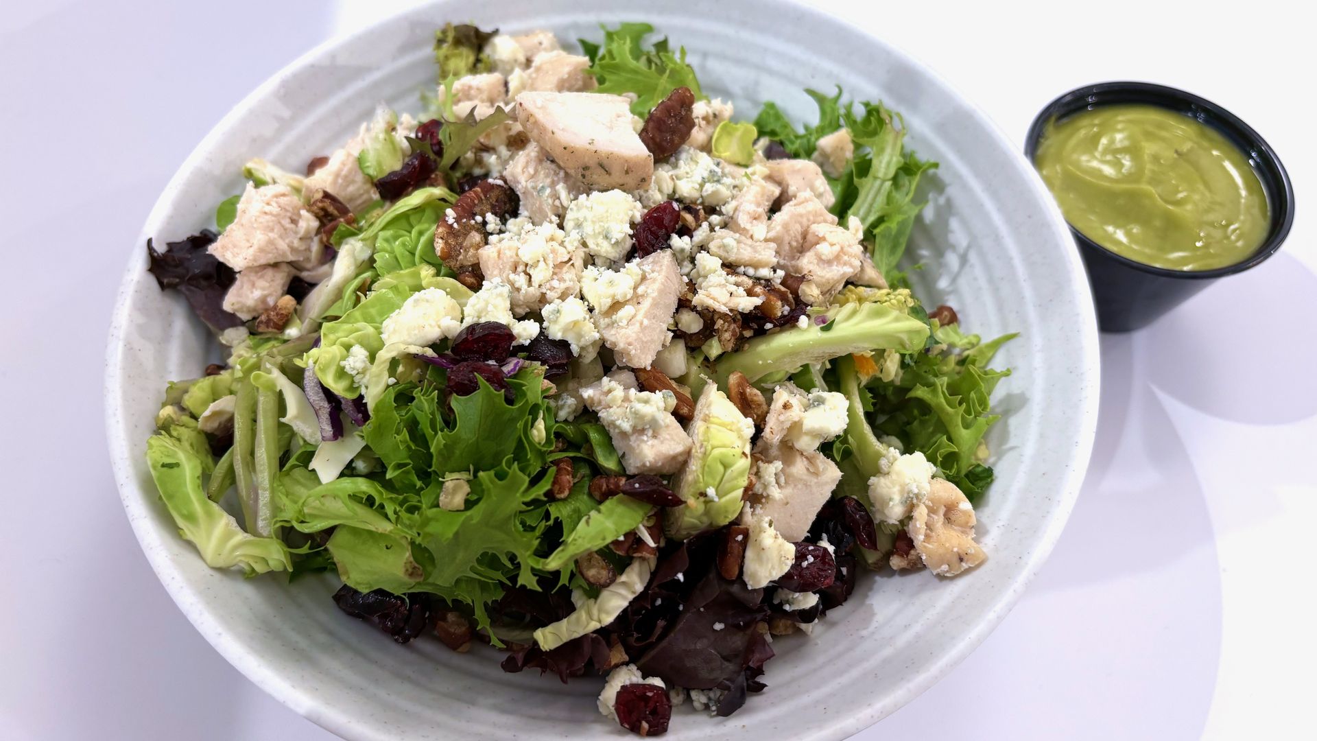 A close-up of a salad topped with bleu cheese and grilled chicken, with a lime-green dressing cup next to it