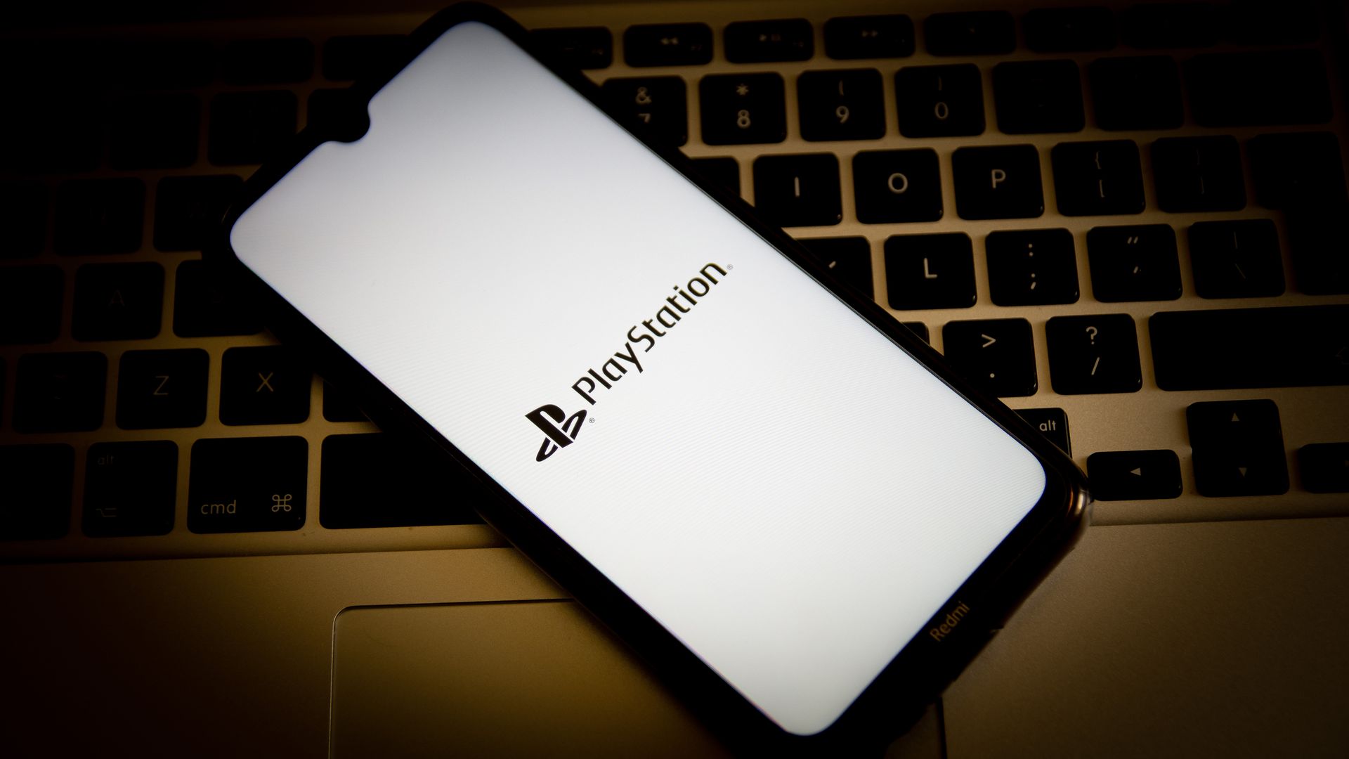 Photo illustration of a phone with a PlayStation logo resting on a keyboard