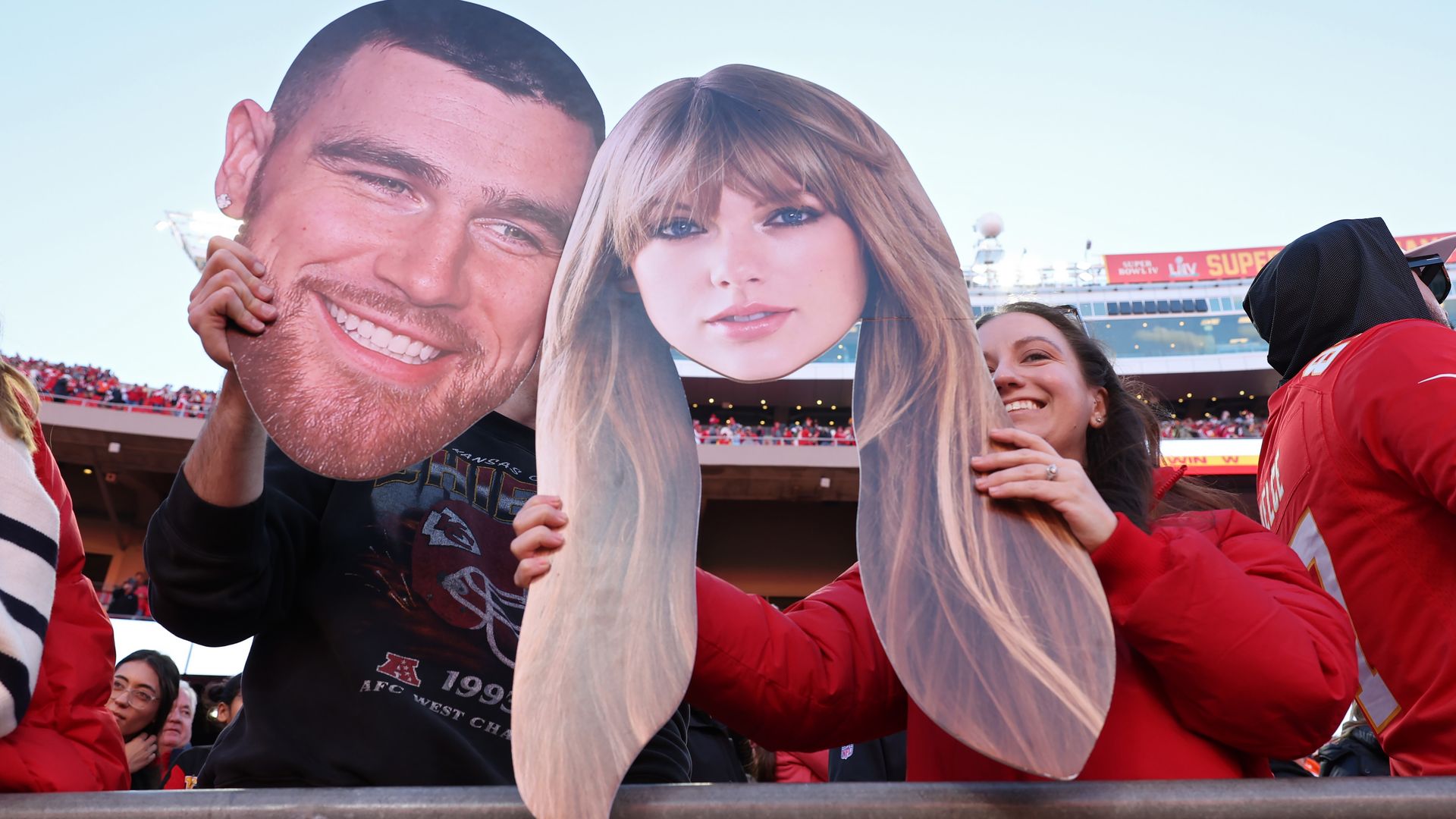 Kansas City Chiefs fans hold up signs of Travis Kelce and Taylor Swift at Arrowhead Stadium.