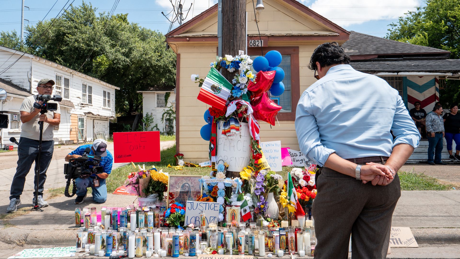 A photo of a man in a blue shirt looking at a vigil on a street that is decked in flowers and prayer candles.