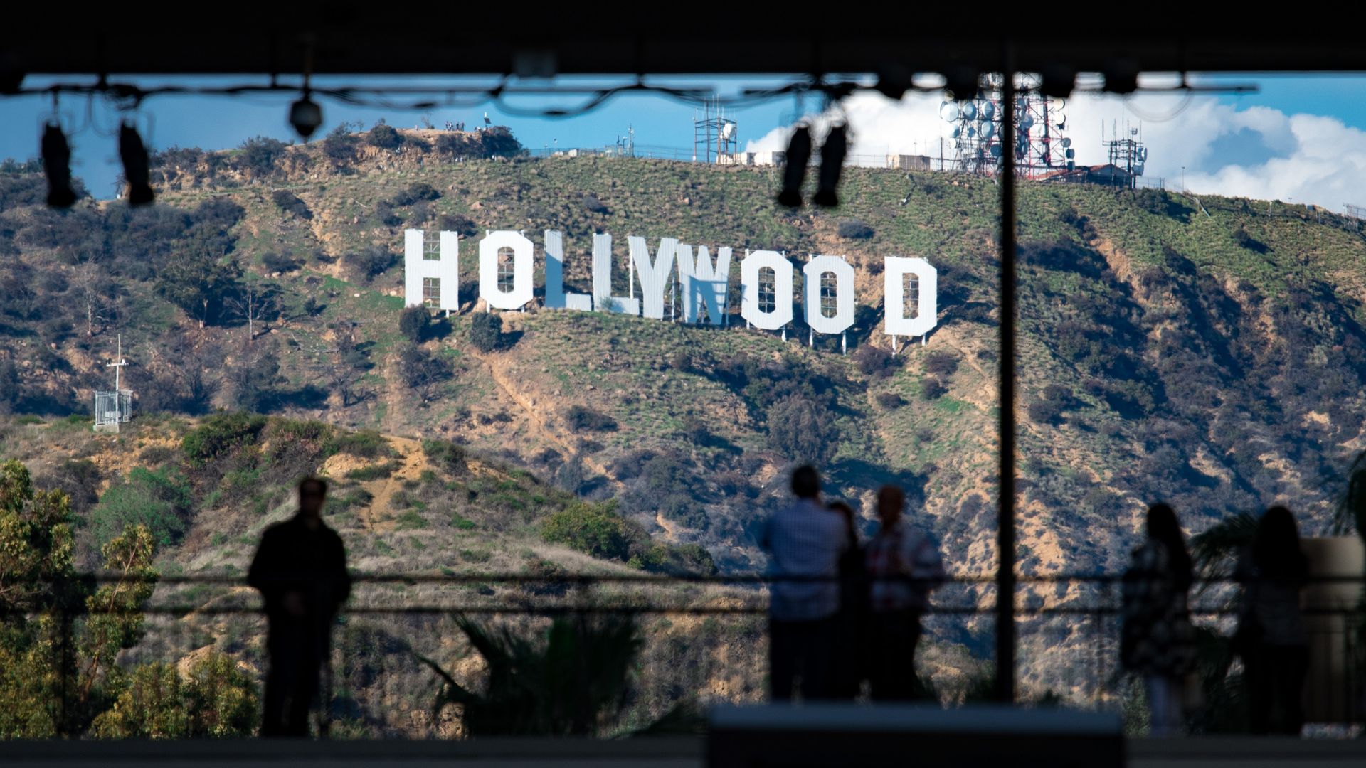 In this image, the Hollywood sign is visible in the background as a man stands and looks at it. 