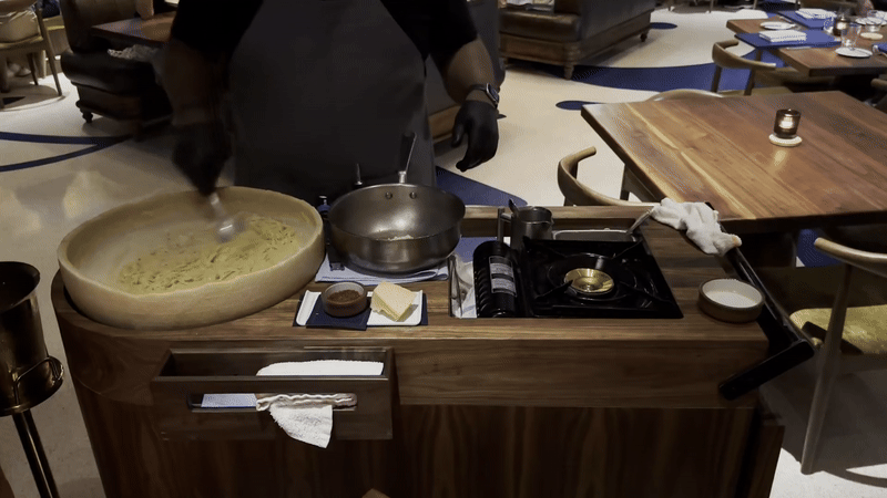 A server swirls pasta around inside a large melting cheese wheel.