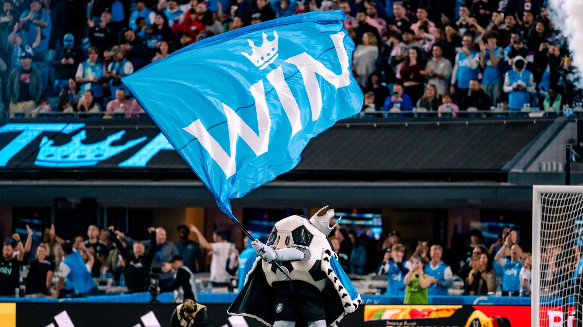 A soccer ball mascot waving a giant blue flag with the word "Win" on it