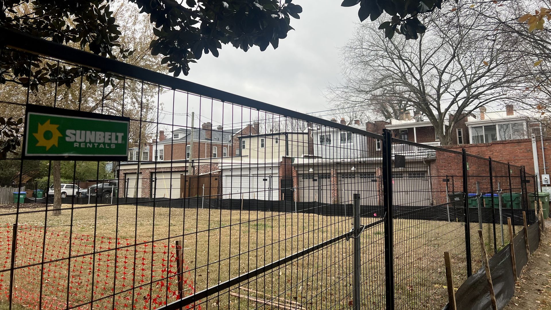 A construction fence lined up against a grassy field in front of houses