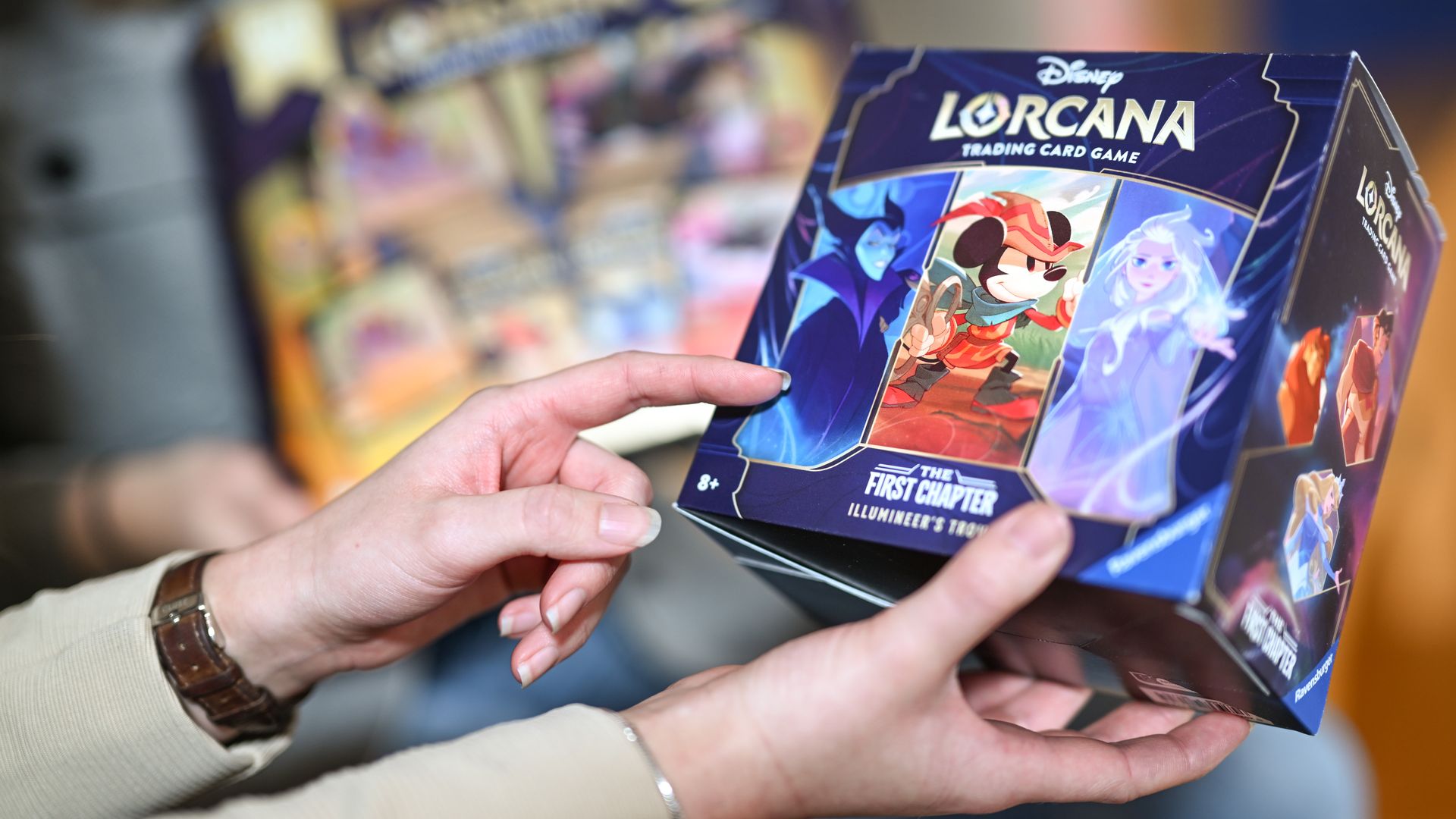 A woman holds a box containing the new Disney Lorcana trading card game.