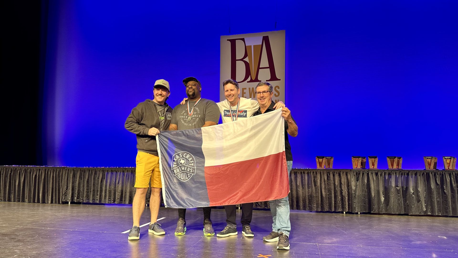 Workers at True Anomaly Brewing hold a flag while celebrating their win at the Great American Beer Festival