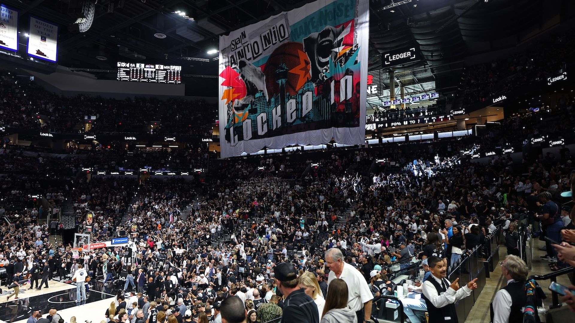 View of fans inside the Frost Bank Center during a Spurs game with a large themed flag in the middle.