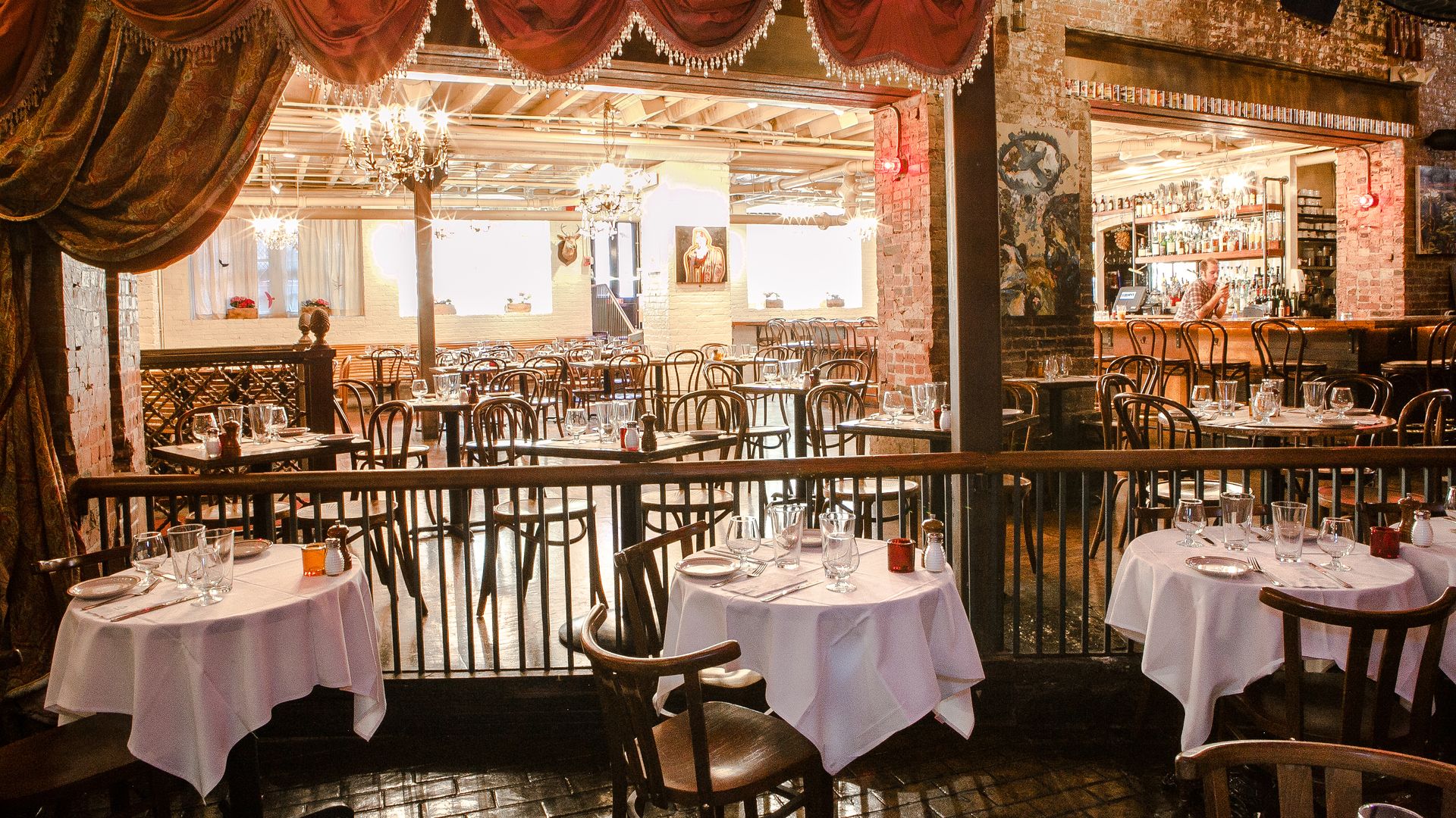 The downstairs dining area at The Beehive restaurant in Boston, with several round tables with white table cloth and wooden chairs.