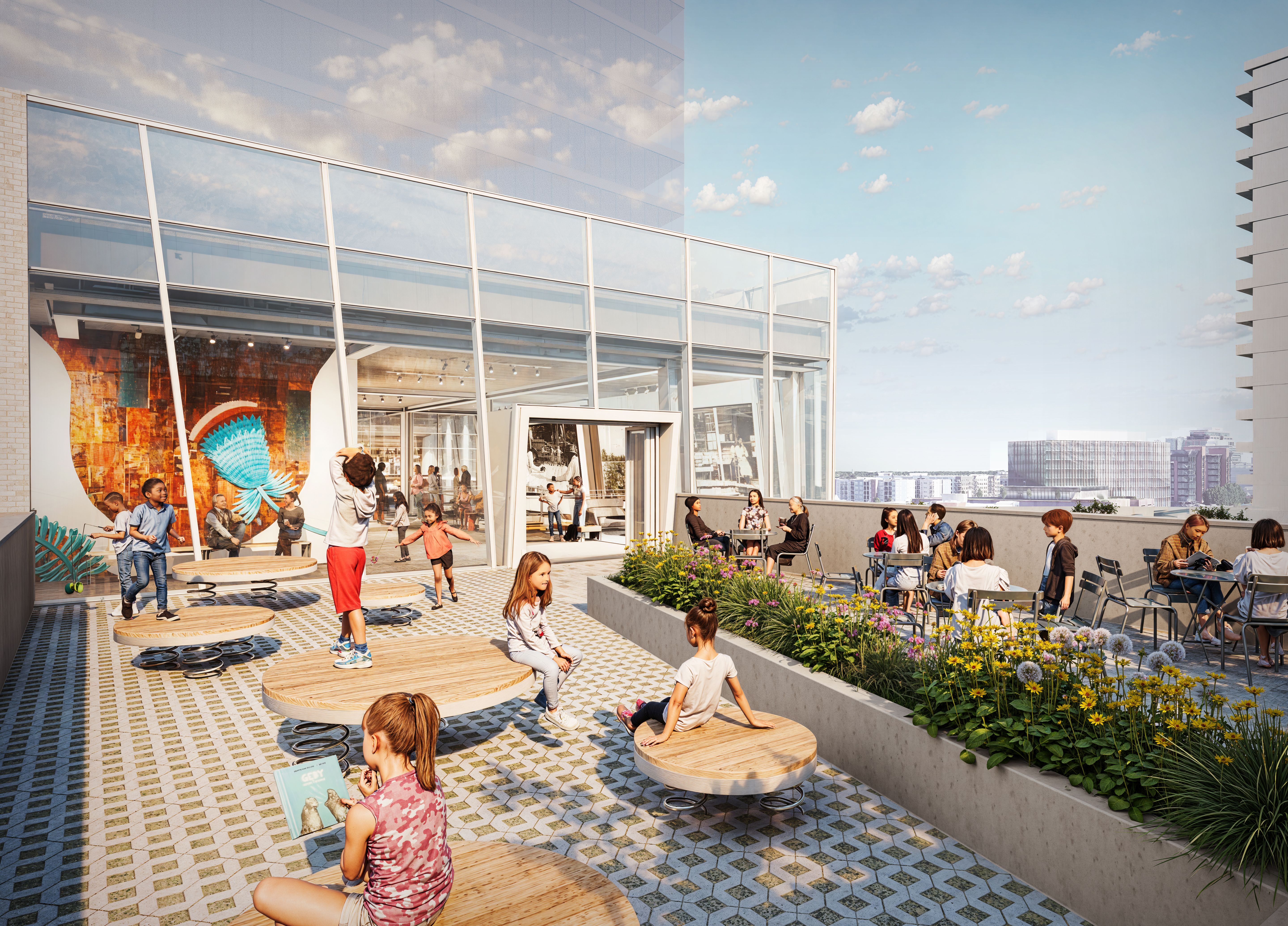 Children playing and sitting on circular wooden platforms, with some adults and kids seated at tables along a flower-lined terrace under a blue sky with scattered clouds.