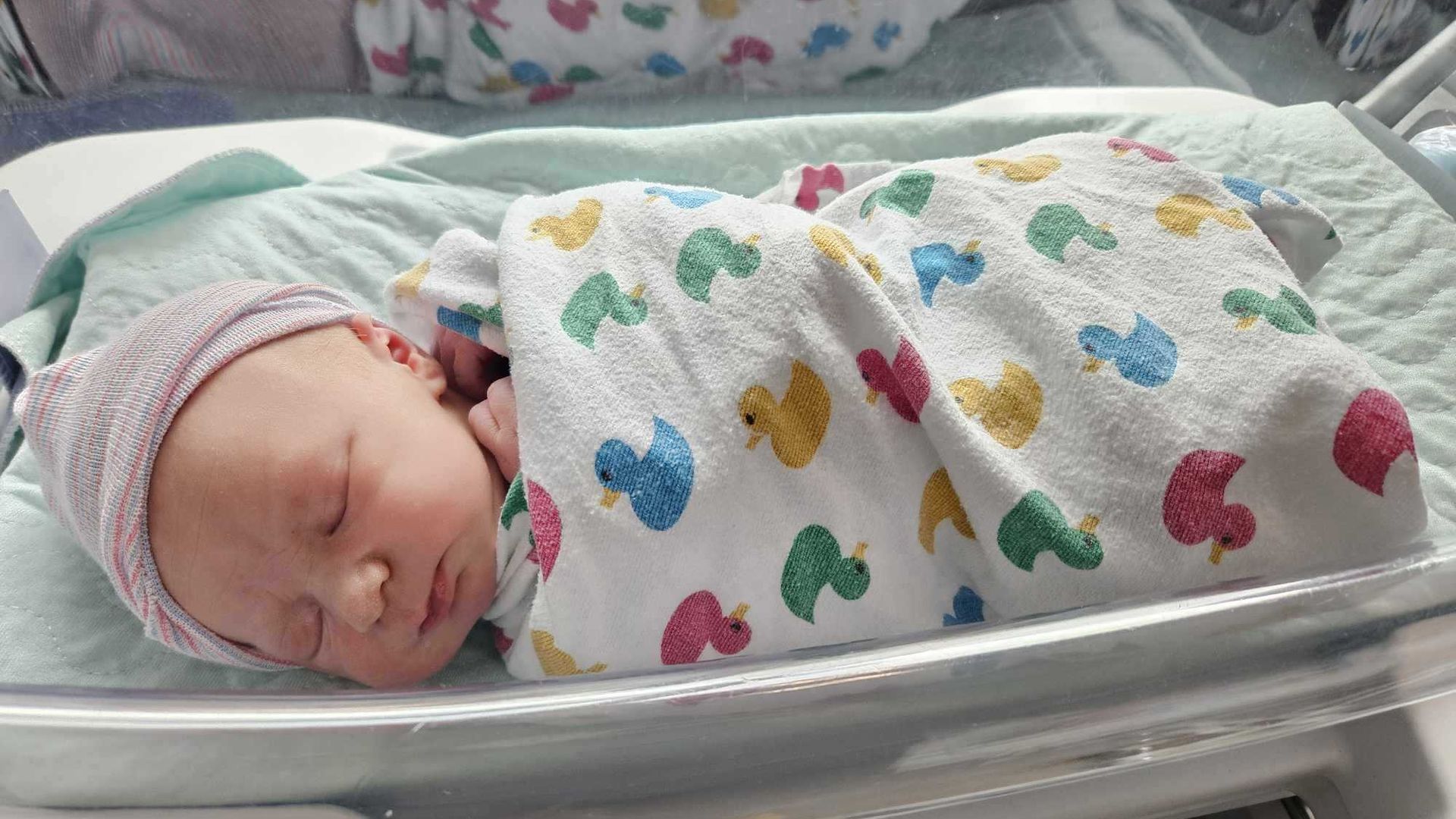 A newborn sits in a hospital crib. 