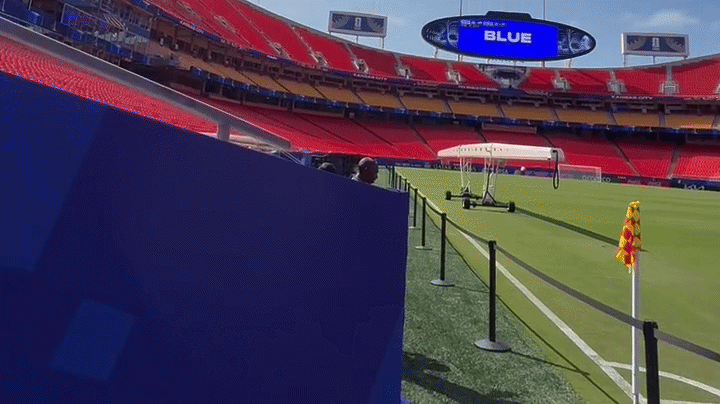 Video pans right and left showing the inside of a stadium in Kansas City with red seats and a soccer field painted on the turf, including a corner kick flag in the foreground and goals in the background.