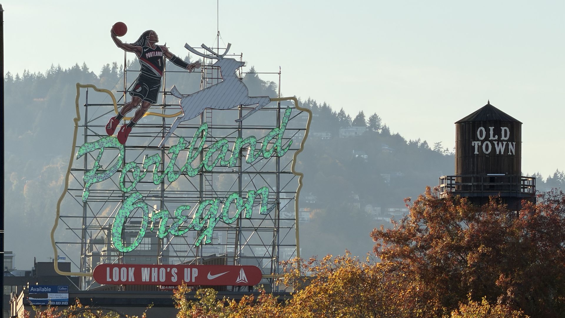 A large neon Portland, Oregon sign shows a leaping basketball player and a white horse, with autumn trees in the foreground and a silo labeled OLD TOWN to the right.