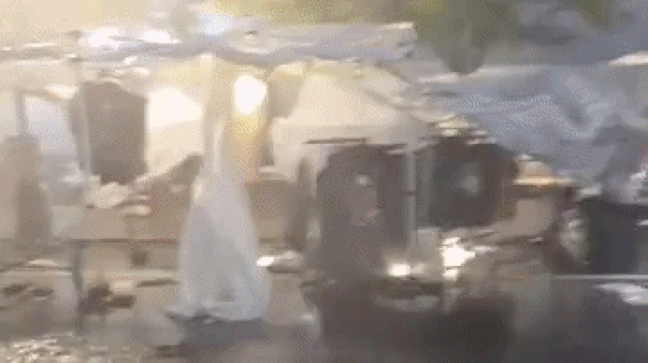Blurry outdoor market scene: tents and clothing are whipped by wind and rain.
