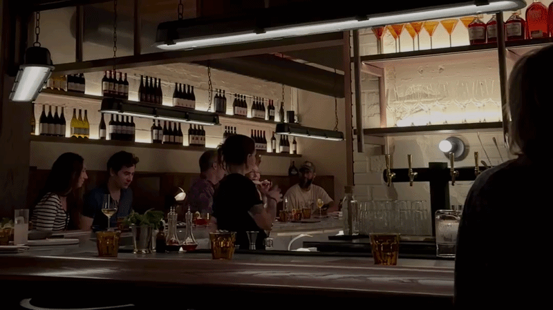 A video inside a moody cocktail bar. The bartender is walking around as people sit around the bar.