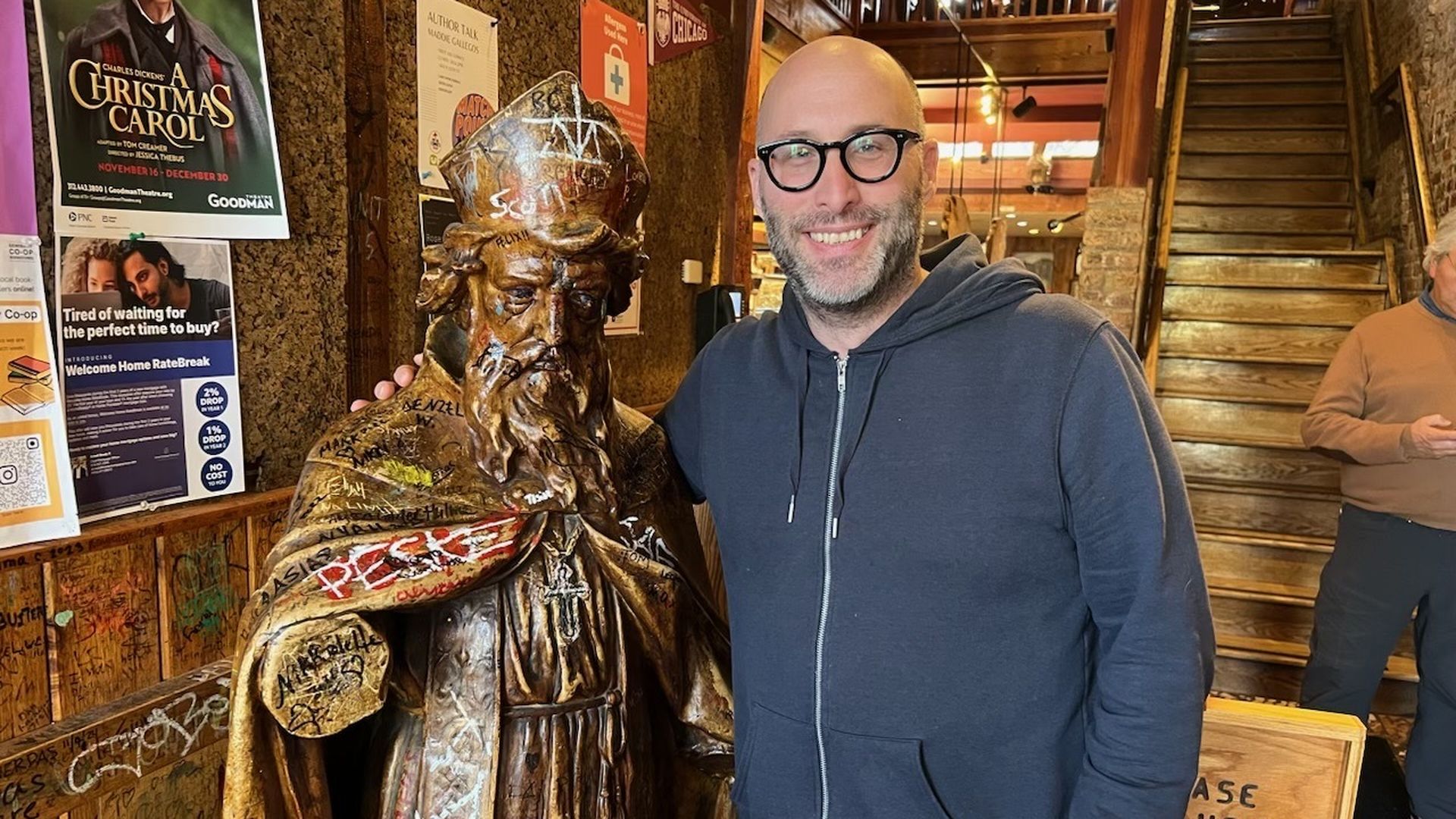 Photo of a man standing next to a statue in a vestibule of a cafe. 