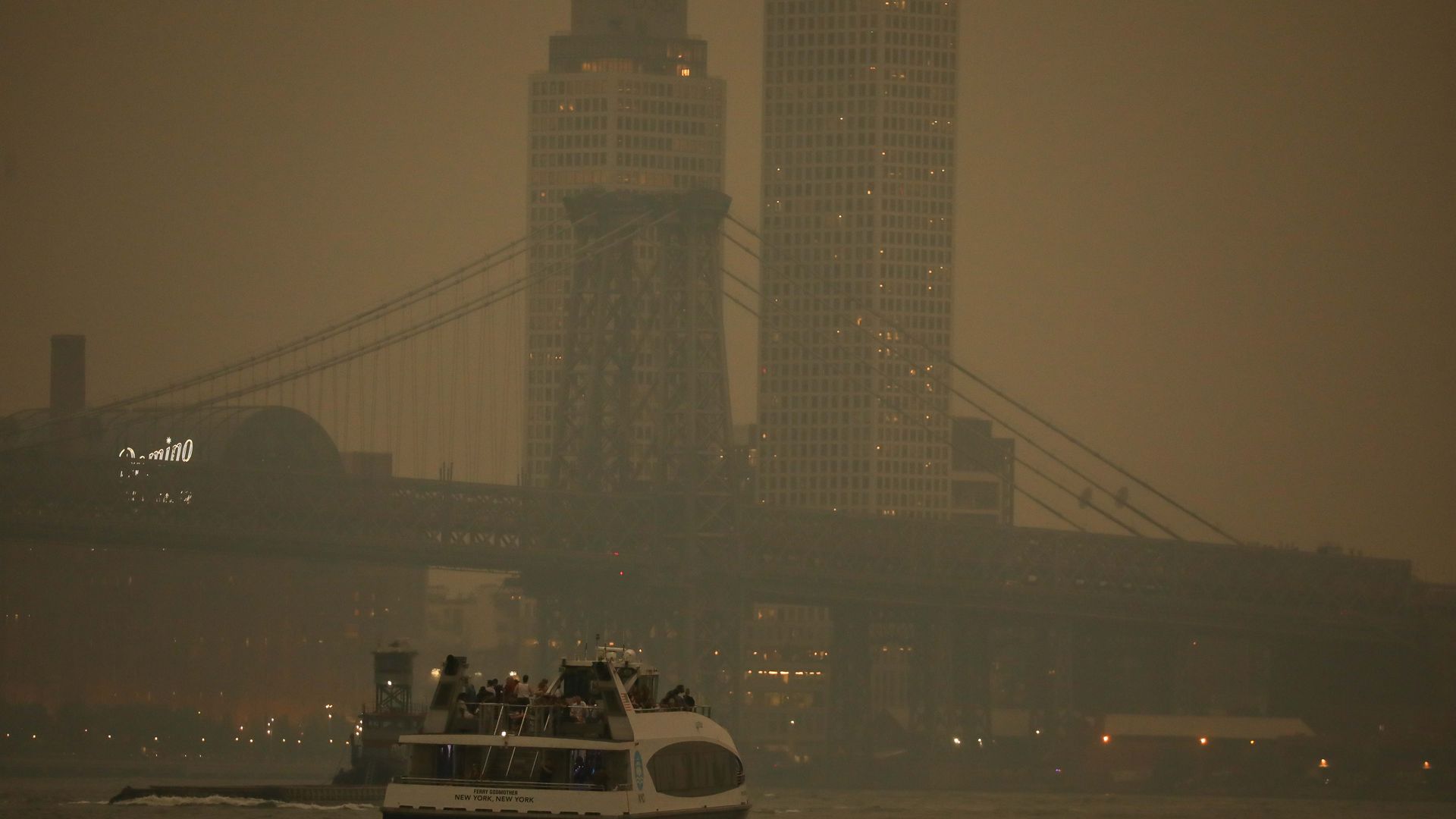 An NYC Ferry travels through heavy wildfire smoke on the East River in Brooklyn, with the Manhattan skyline obscured by haze caused by smoke drifting south from Canadian wildfires.