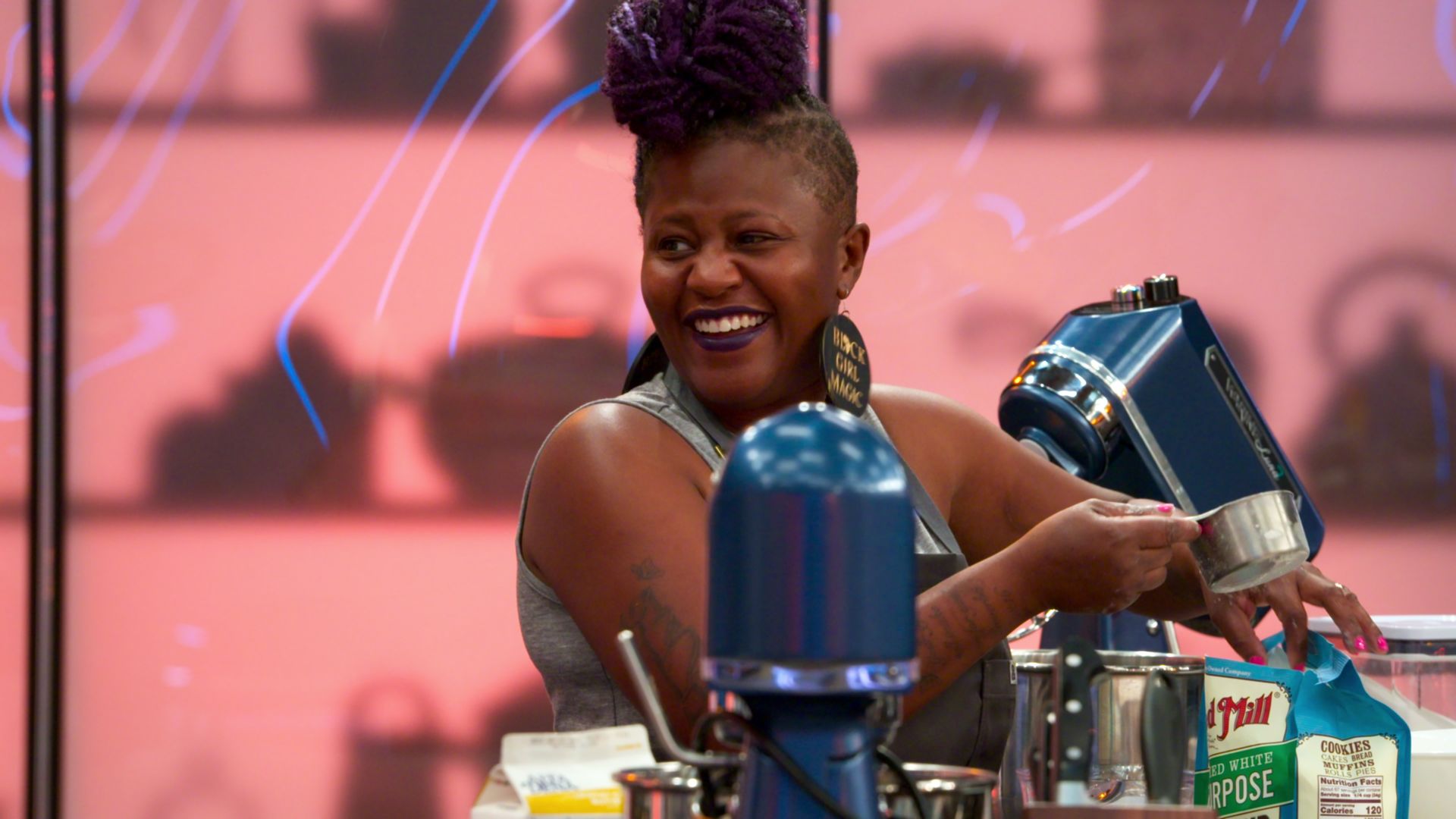 A woman with awesome hair smiles as she loads ingredients into a mixer to bake a cake