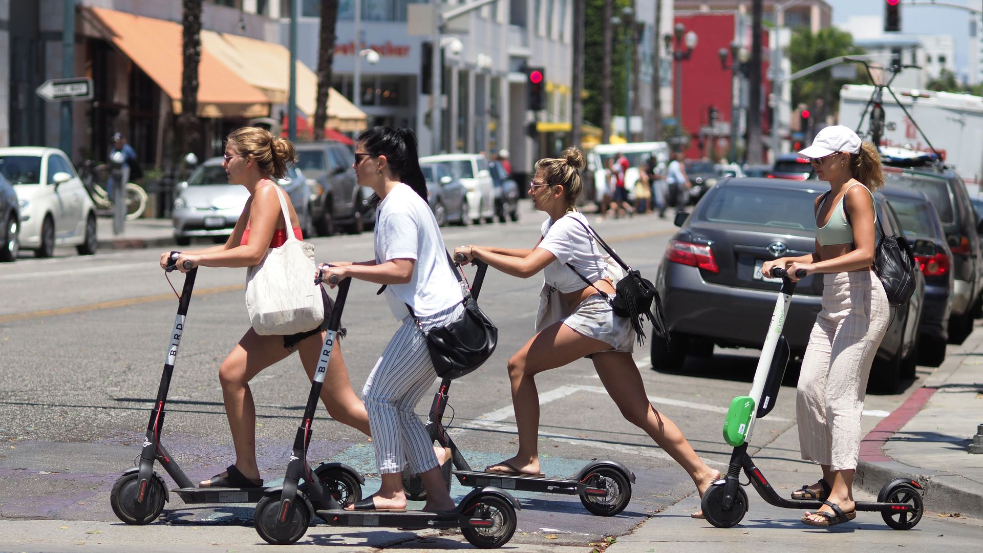 A group of women riding electric scooters across a street in Santa Monica