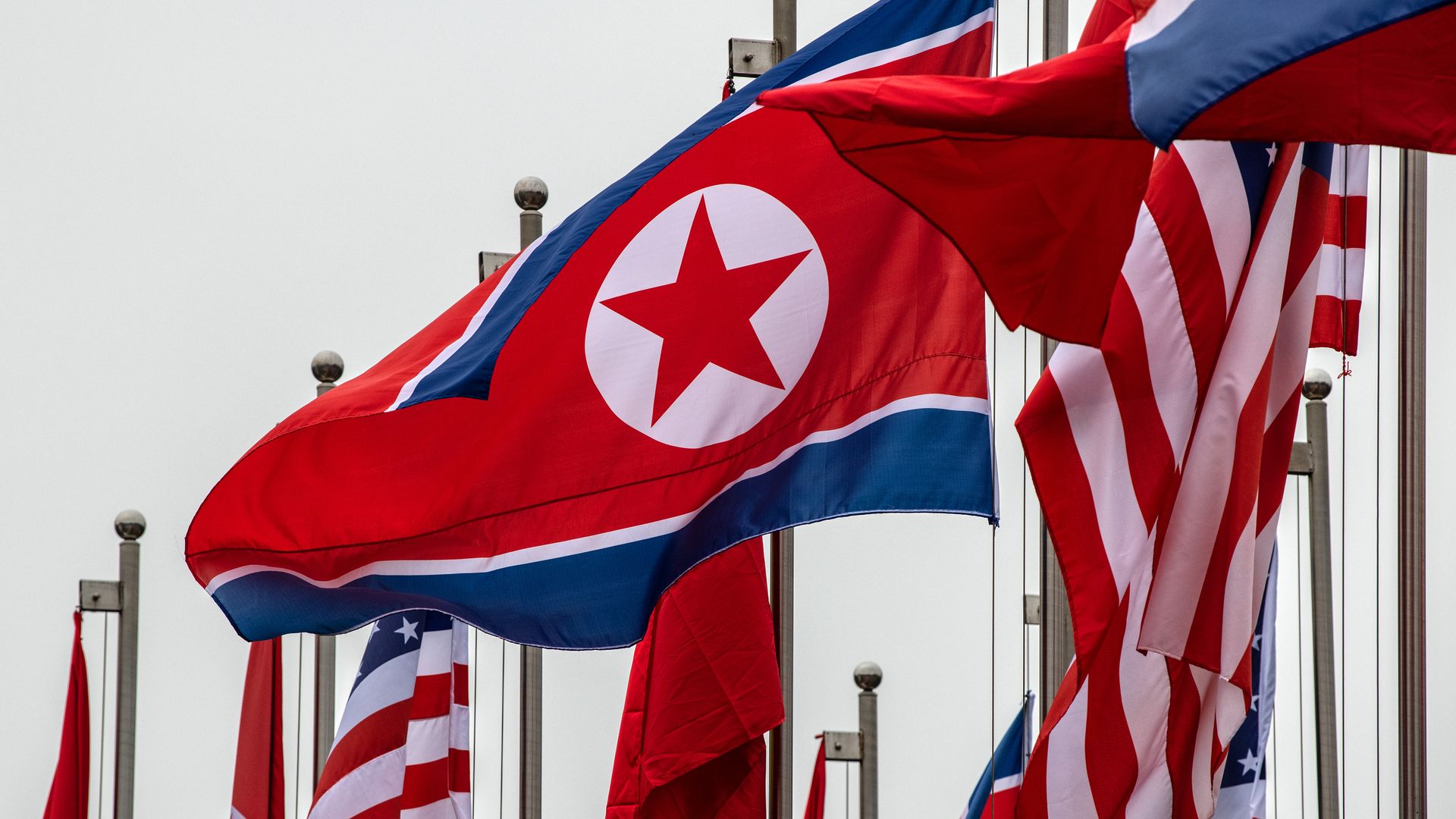In this image, North Korean and US flags wave over each other