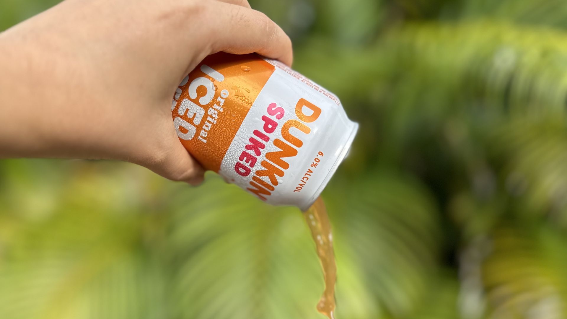A hand pouring out a can of brown liquid from a can labeled "DUNKIN' SPIKED"