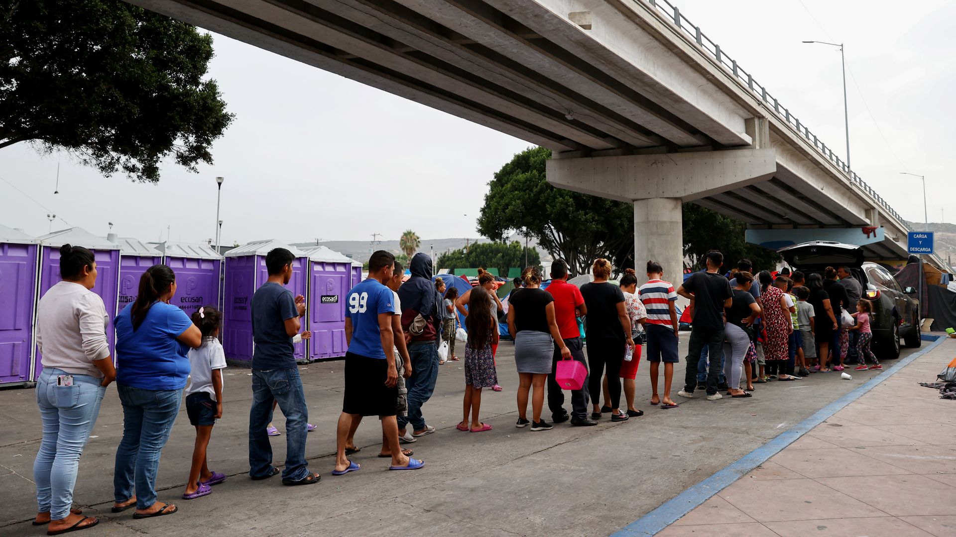 Asylum-seeking migrants wait in line for donated food at a makeshift migrant camp on the Mexican side of the San Ysidro Port of Entry 