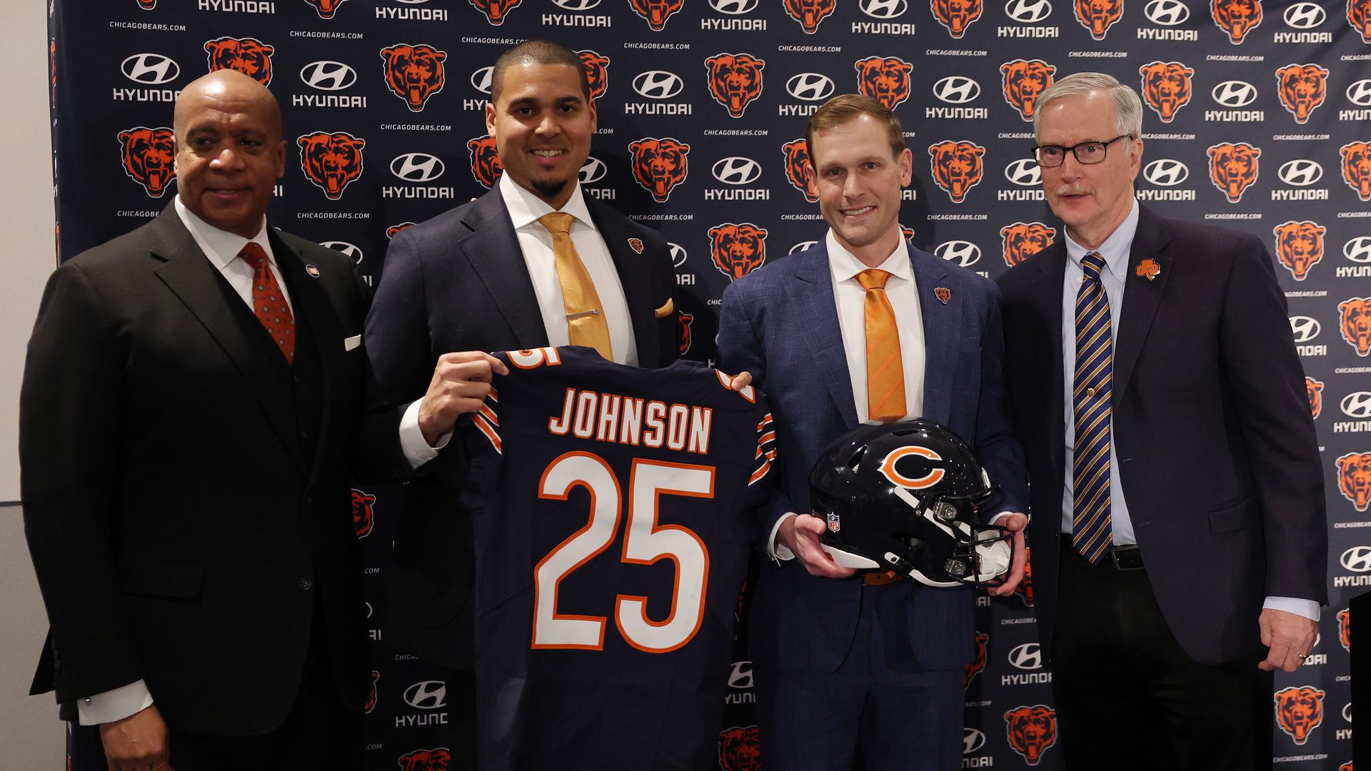 Photo of four men holding a jersey and a helmet. The jersey says "Johnson" on the back. 