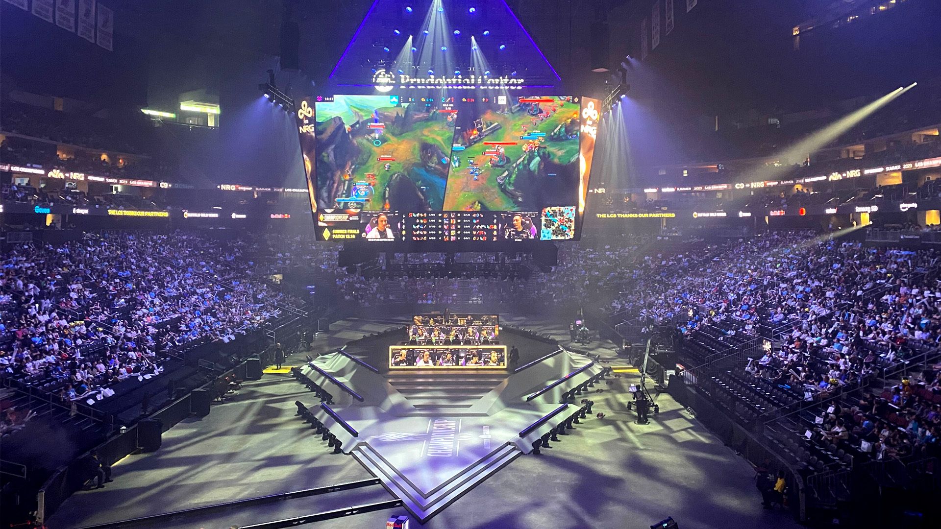 Photo of an arena half-full of people watching a League of Legends match projects on a screen above the teams playing it
