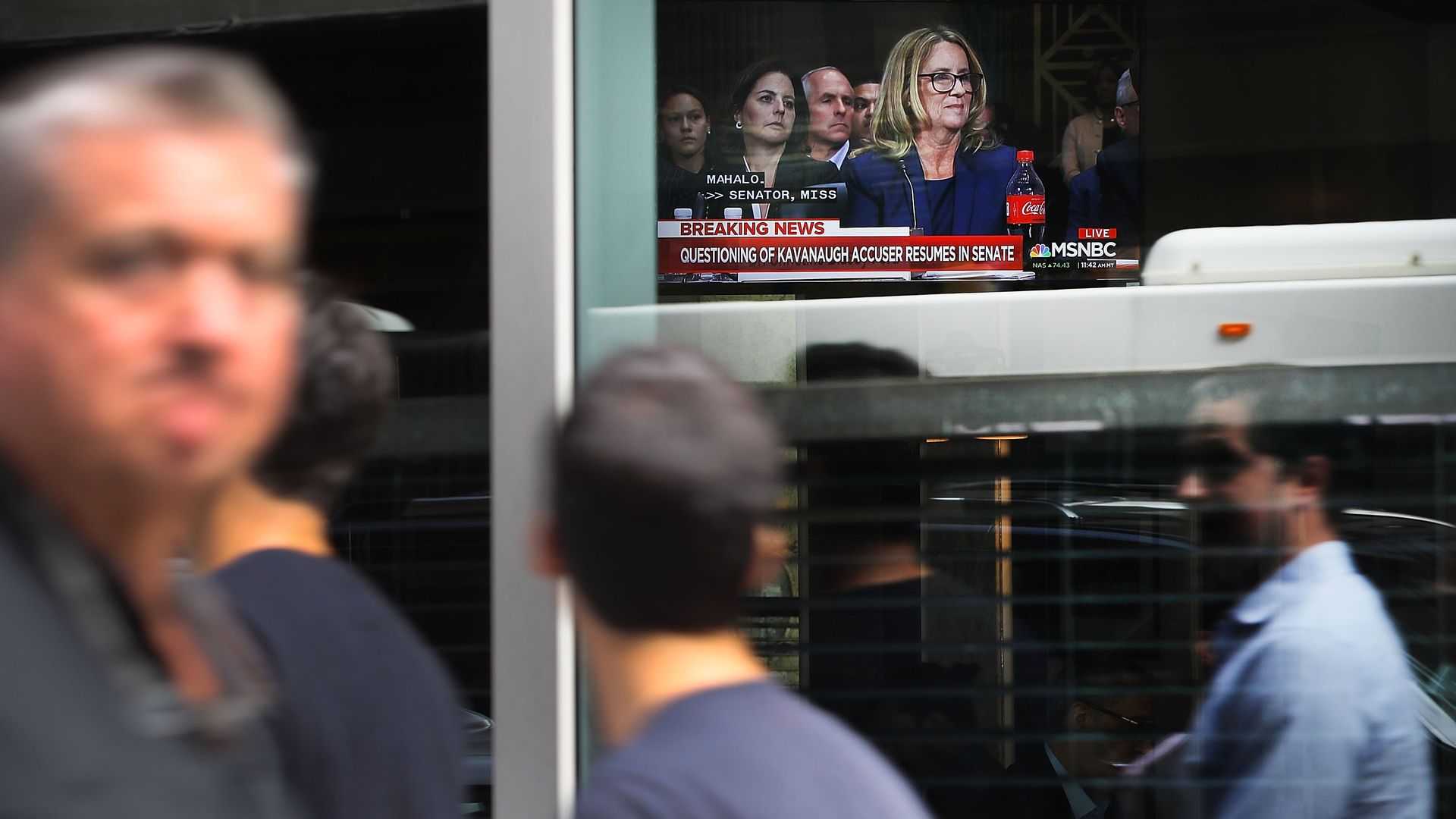 People walk by as the Ford hearing plays on a TV inside a window.
