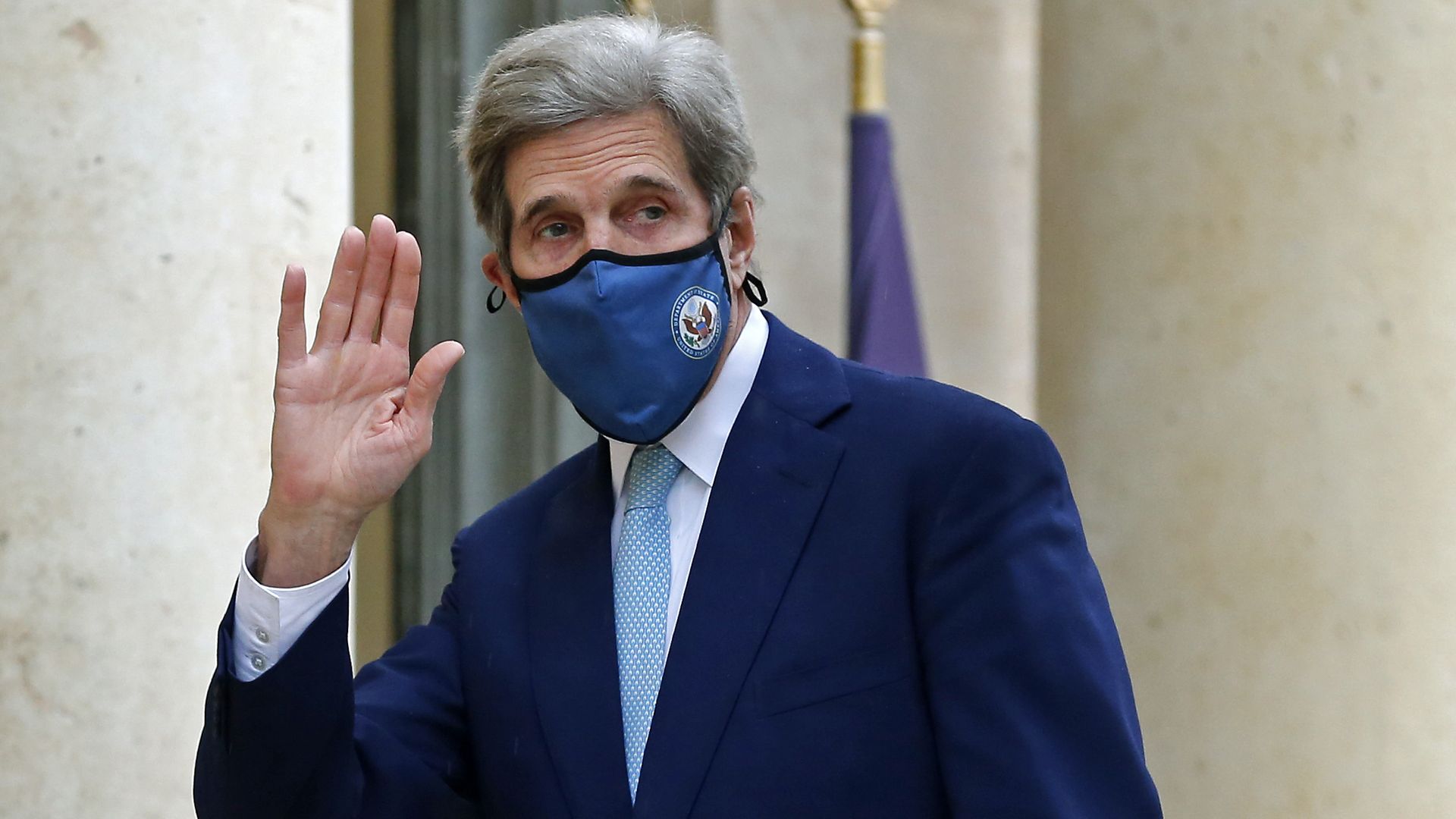 John Kerry wearing a mask and waving at the camera.