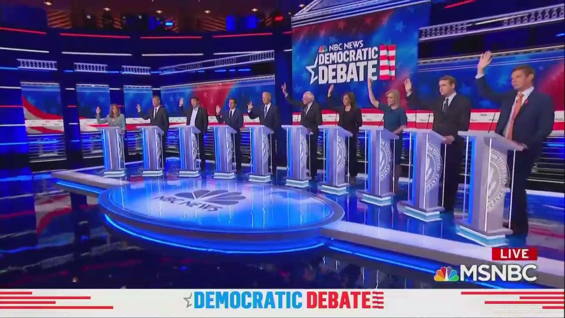 2020 Democratic candidates raise their hands on the debate stage supporting healthcare for undocumented migrants