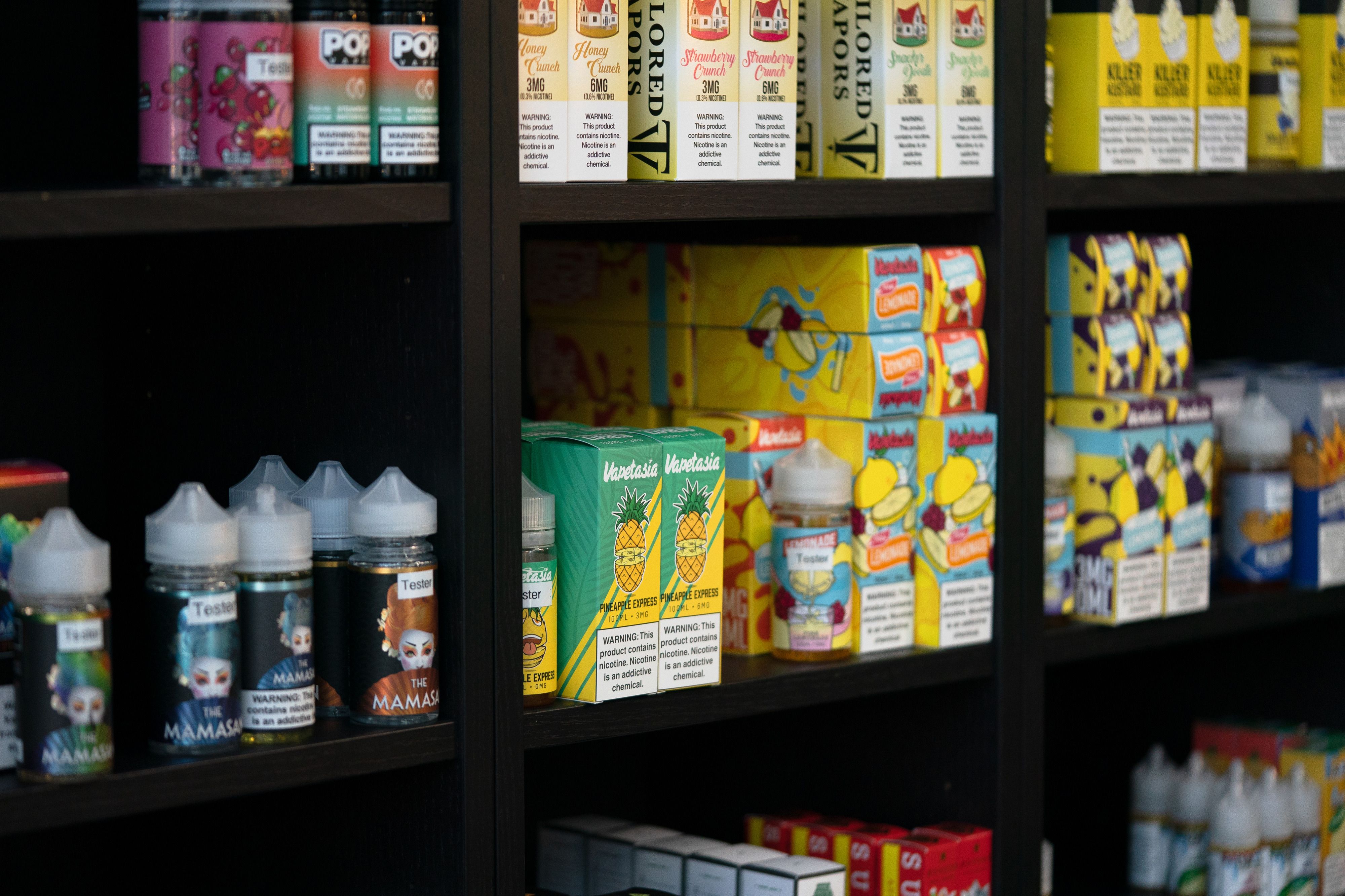 Rows of vaping liquids, some of them flavored, sit on the shelf at a store, in colorful boxes.