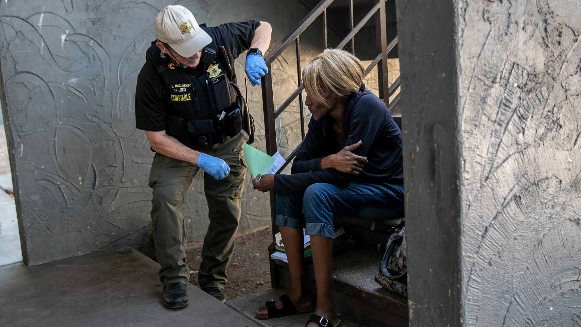 A man in uniform leans down to speak to a woman huddled while sitting on the stairs