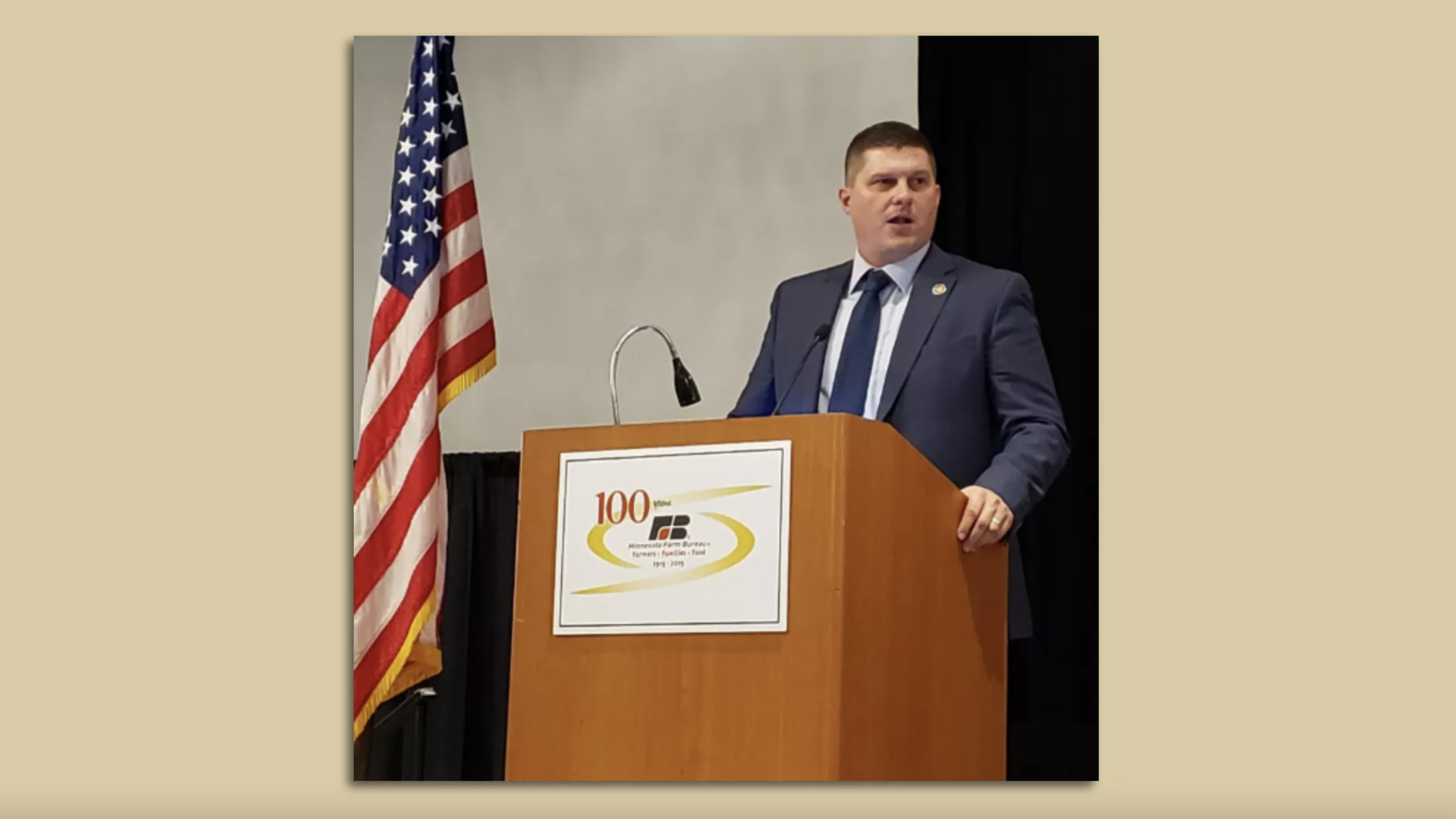 Brad Findstad standing at a podium with a flag next to him