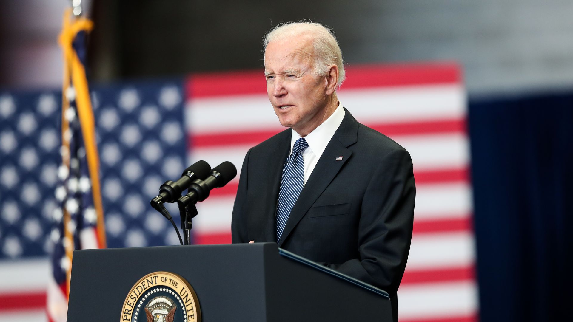 Photo of Joe Biden speaking from a podium with a giant American flag hanging behind him