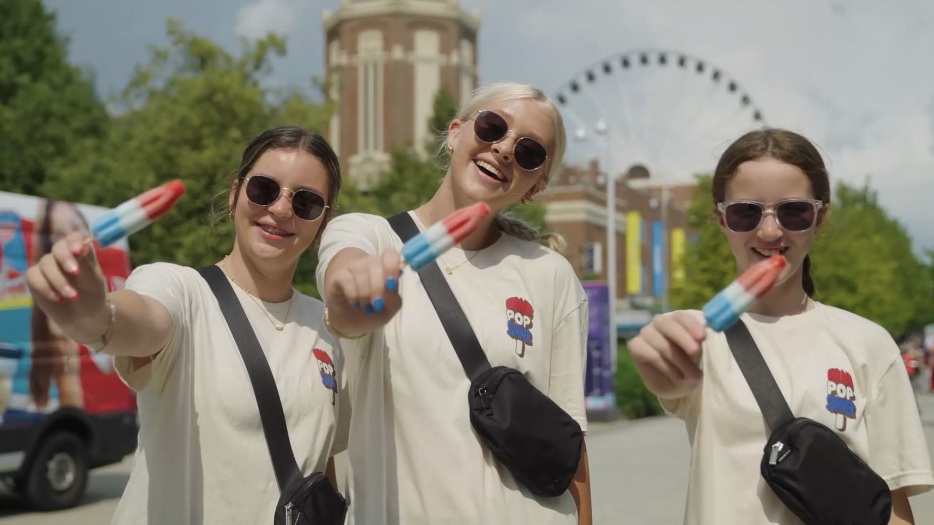 Three women hold up red, white and blue popsicles as they smile toward the camera.