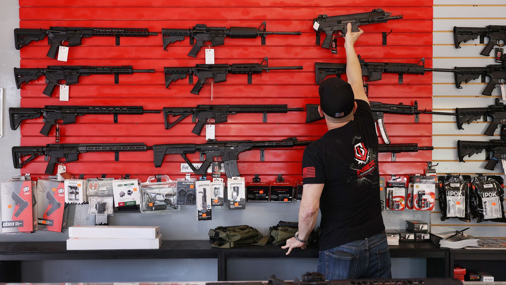 Photo of a person reaching up to take a gun off a rack of firearms
