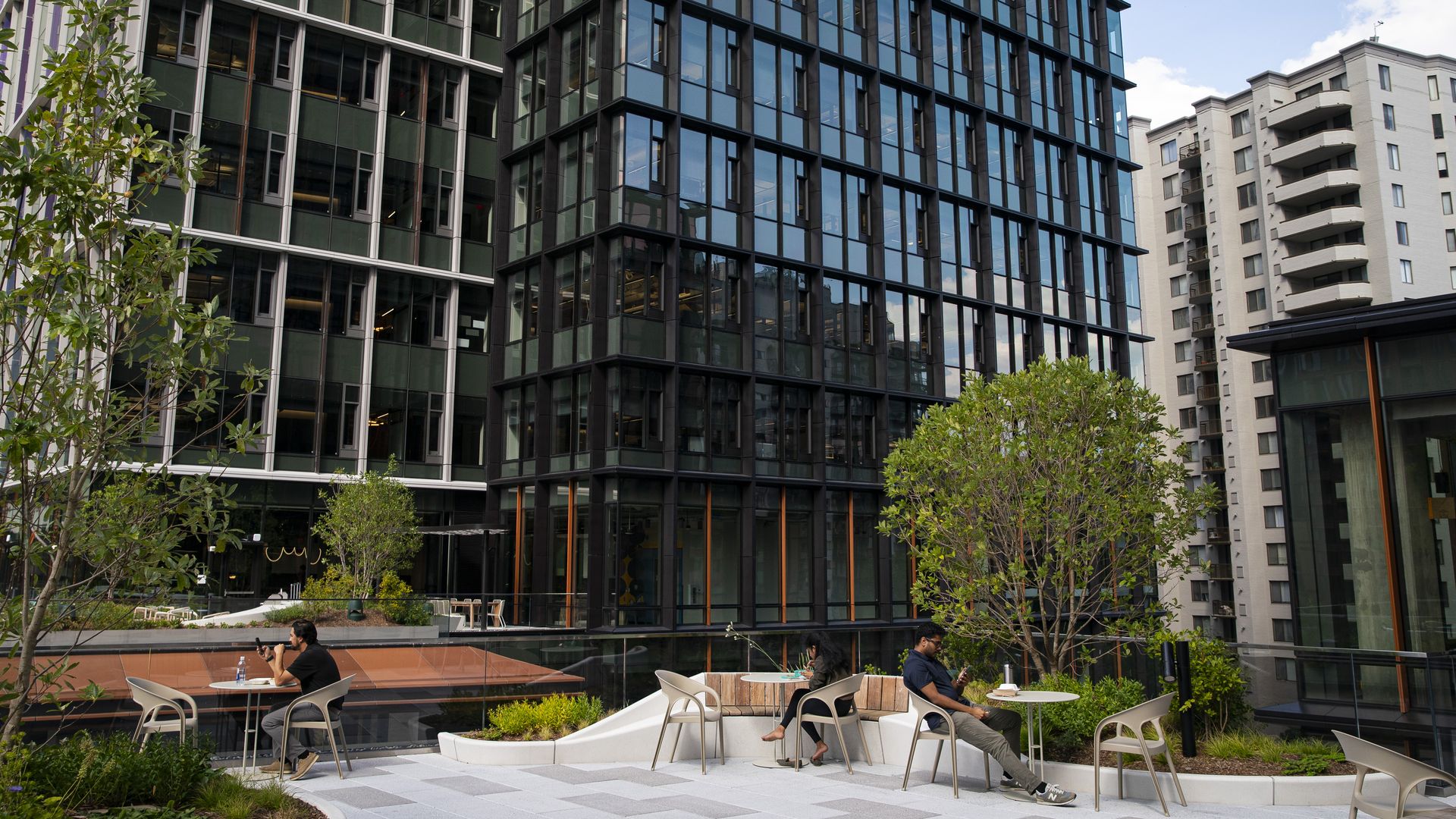 A photo of workers sitting on top of a roof in front of a large office tower.