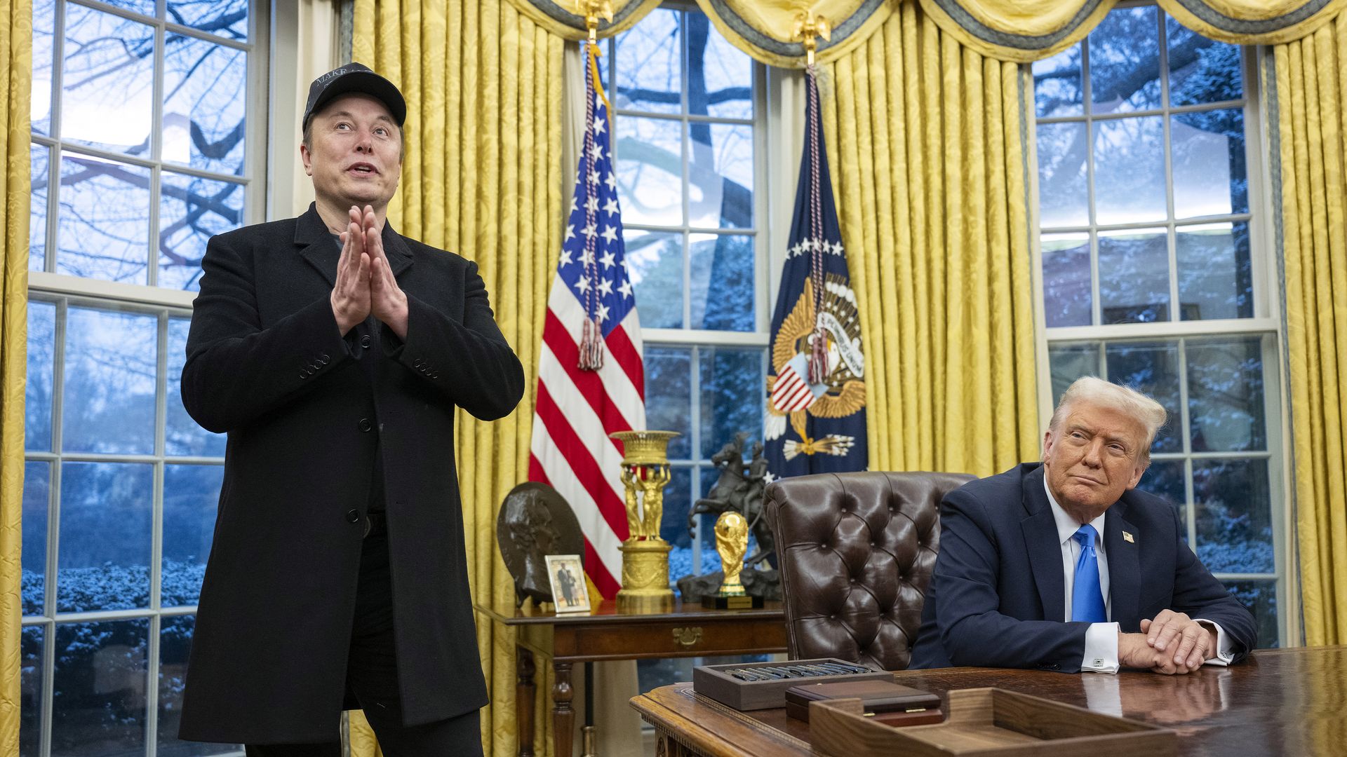 Elon Musk stands as he speaks in the Oval Office as President Trump looks on from his desk.