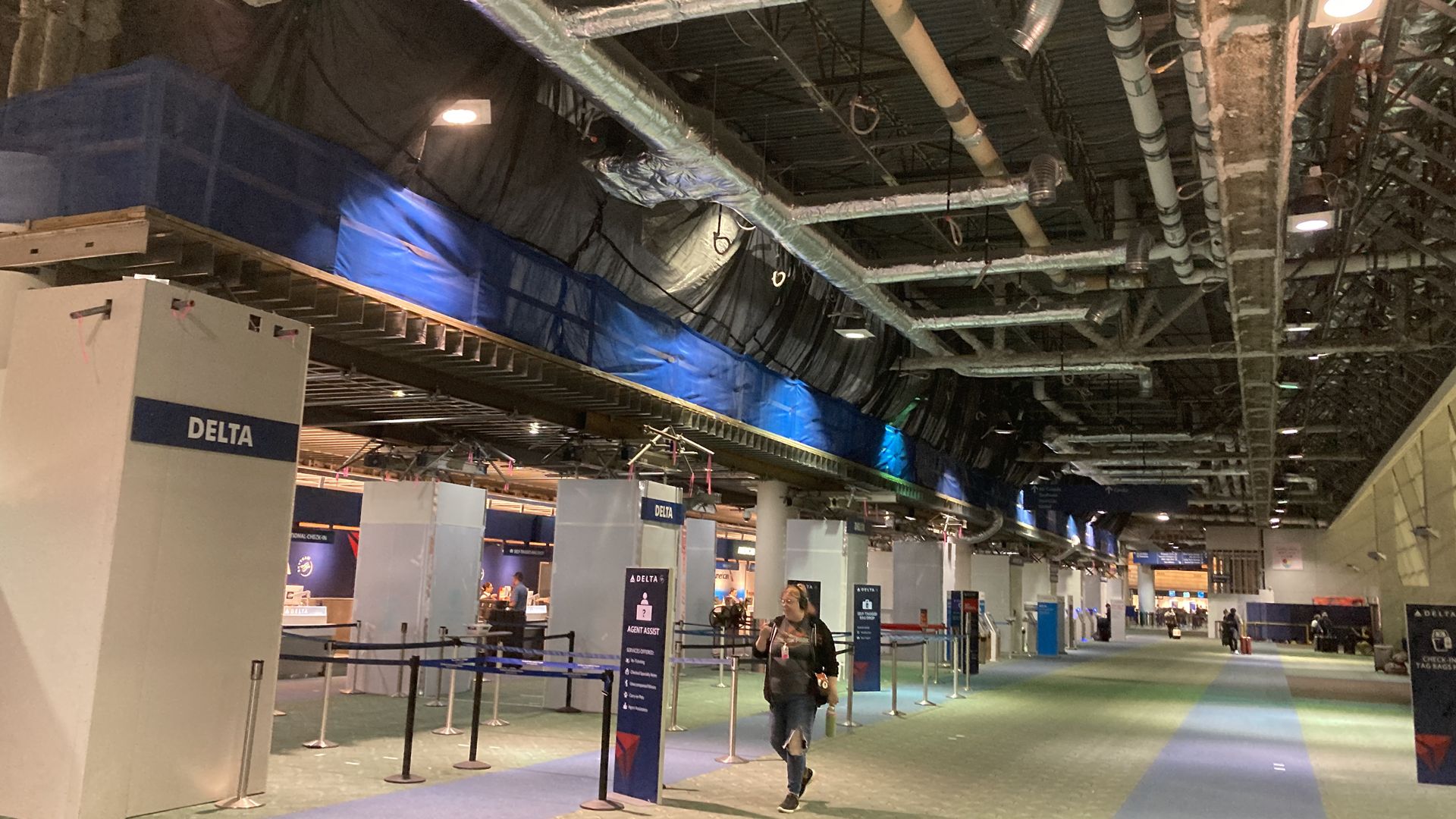 A person walking by airline check-in counters with pipes exposed in the ceiling for reconstruction.