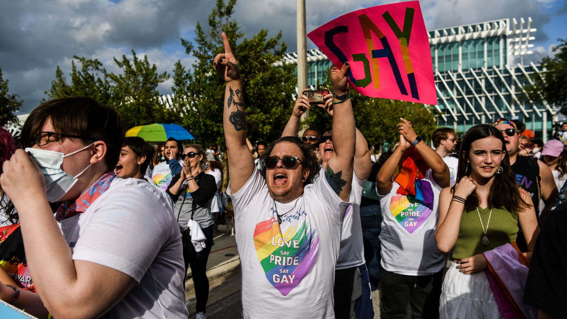 protester holds a sign that says "Gay" wearing a tshirt that says "say love say pride say gay"