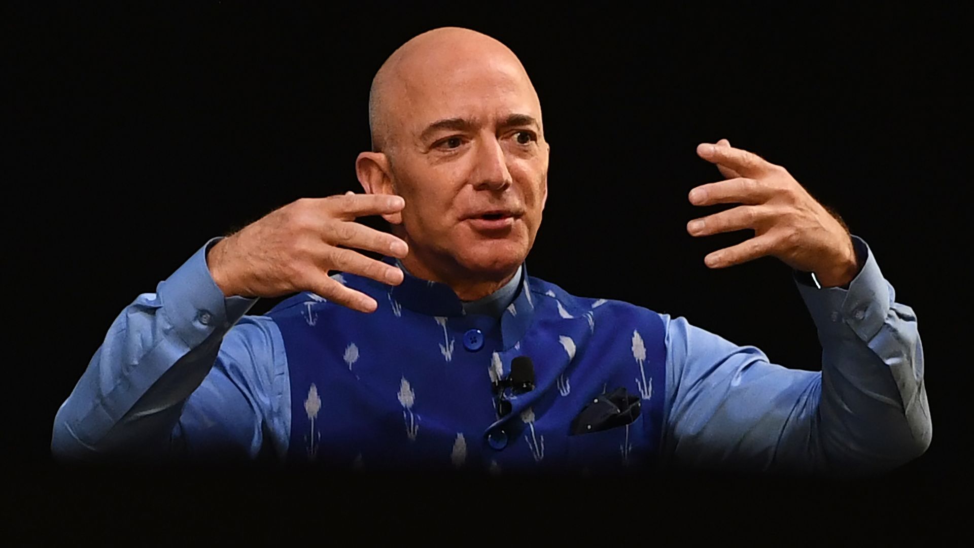 In this image, Bezos sits on stage with his hands in front of his face