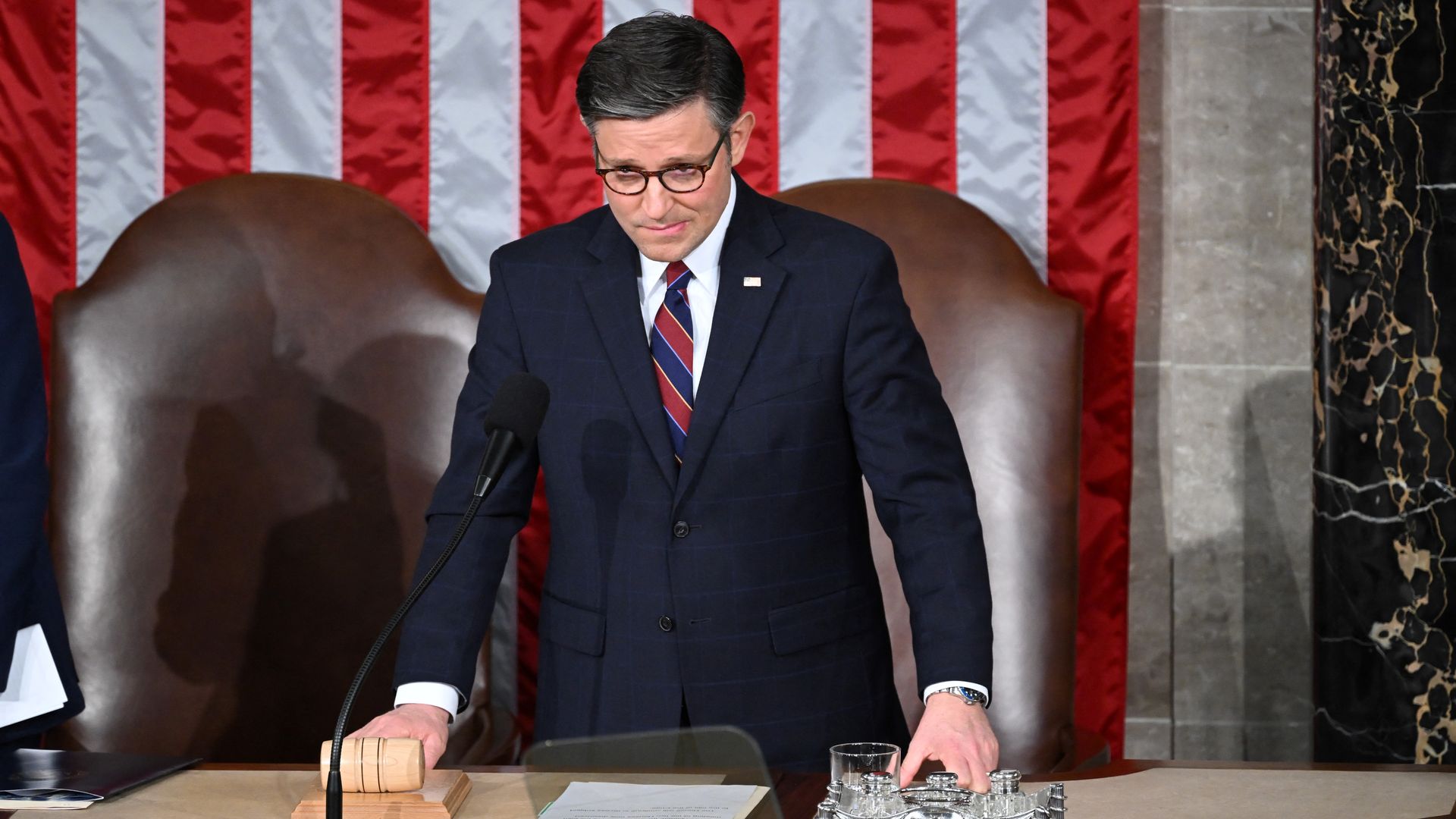 House Speaker Mike Johnson, wearing a blue suit and holding a gavel as he stands in the House chamber.