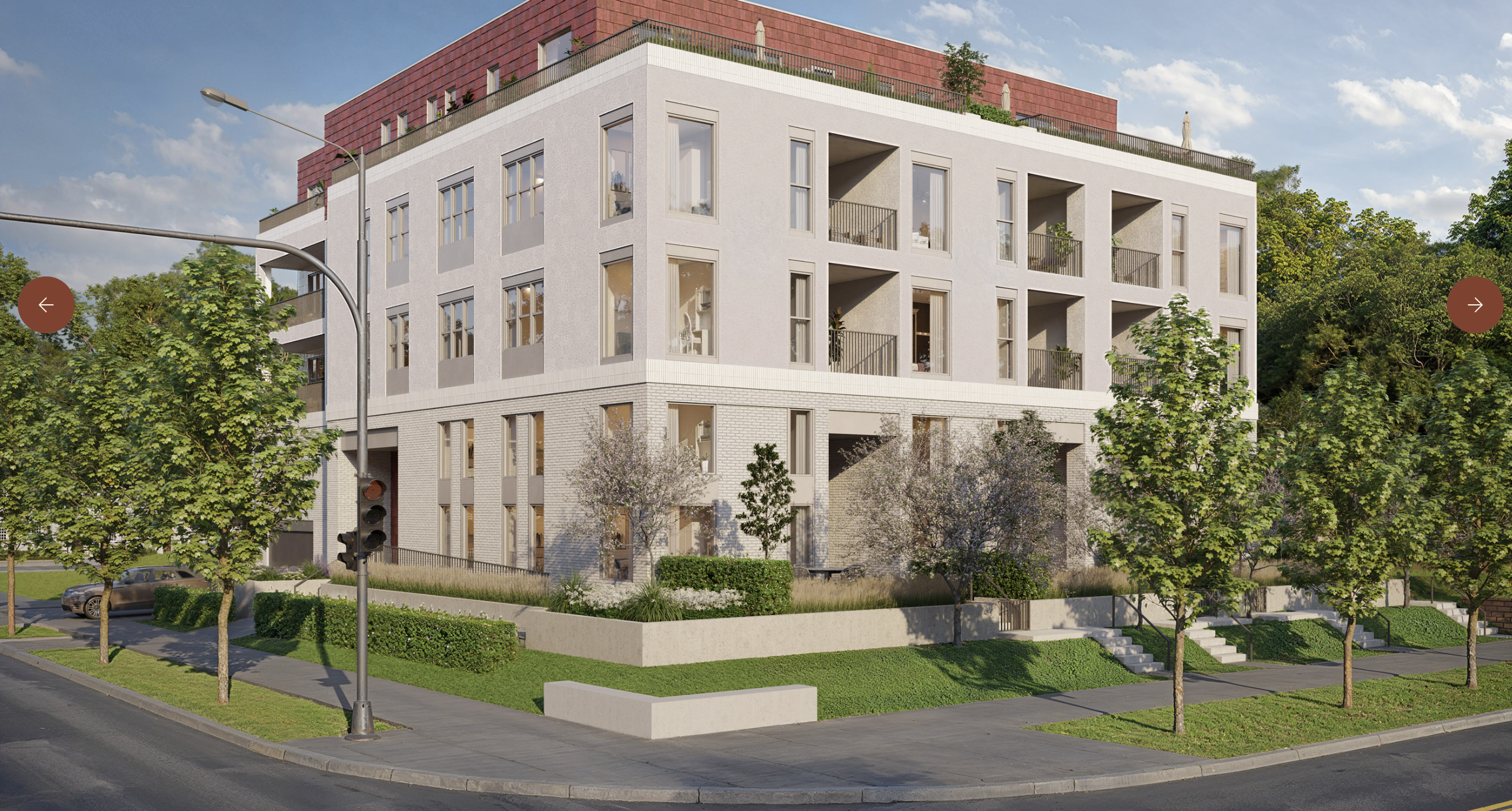 Modern four-story apartment building on a street corner, light gray facade with large windows and recessed balconies, brick-red top, green trees, and a blue sky.