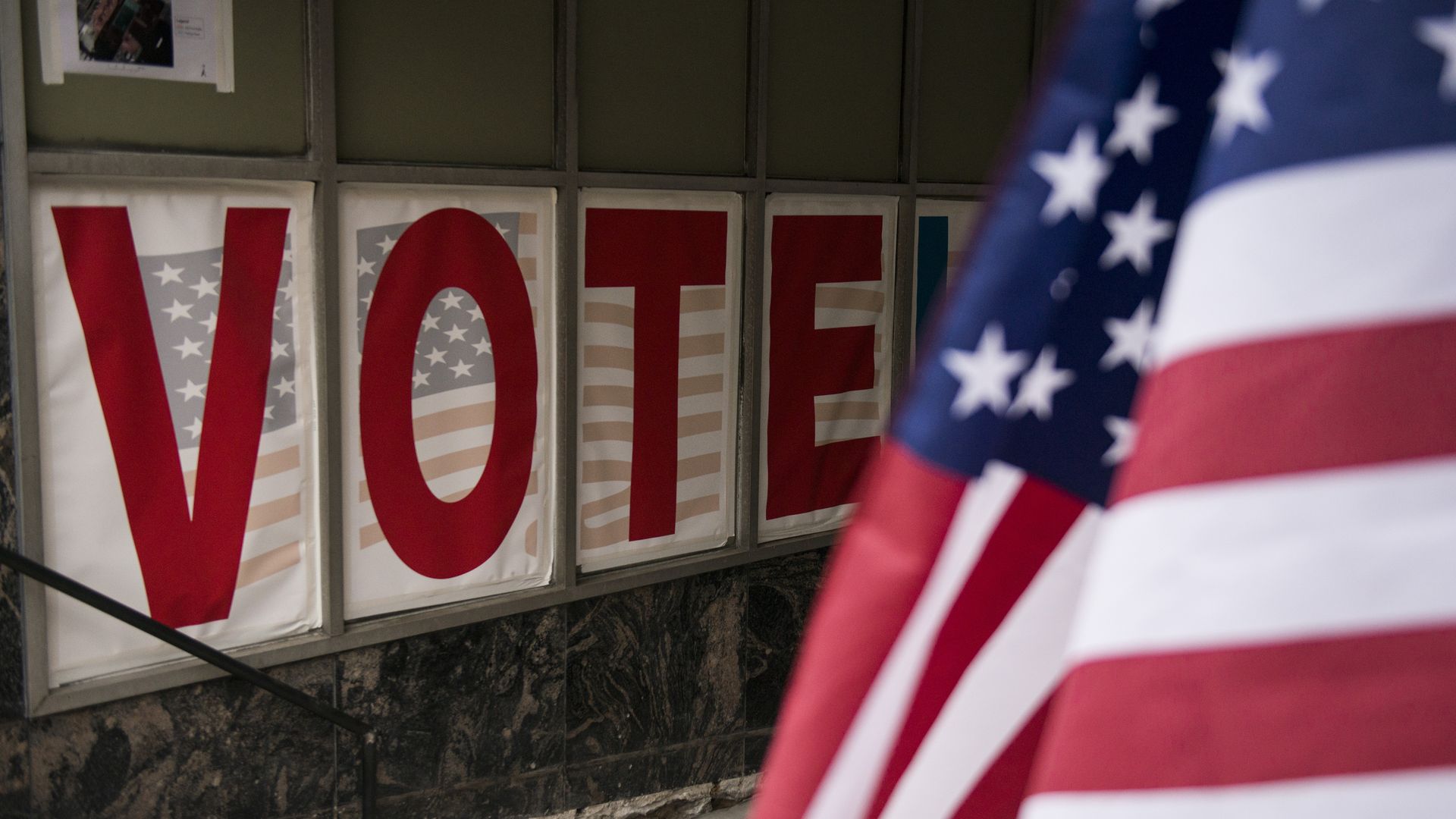 Four large posters with V O T E in red lettering and an American flag