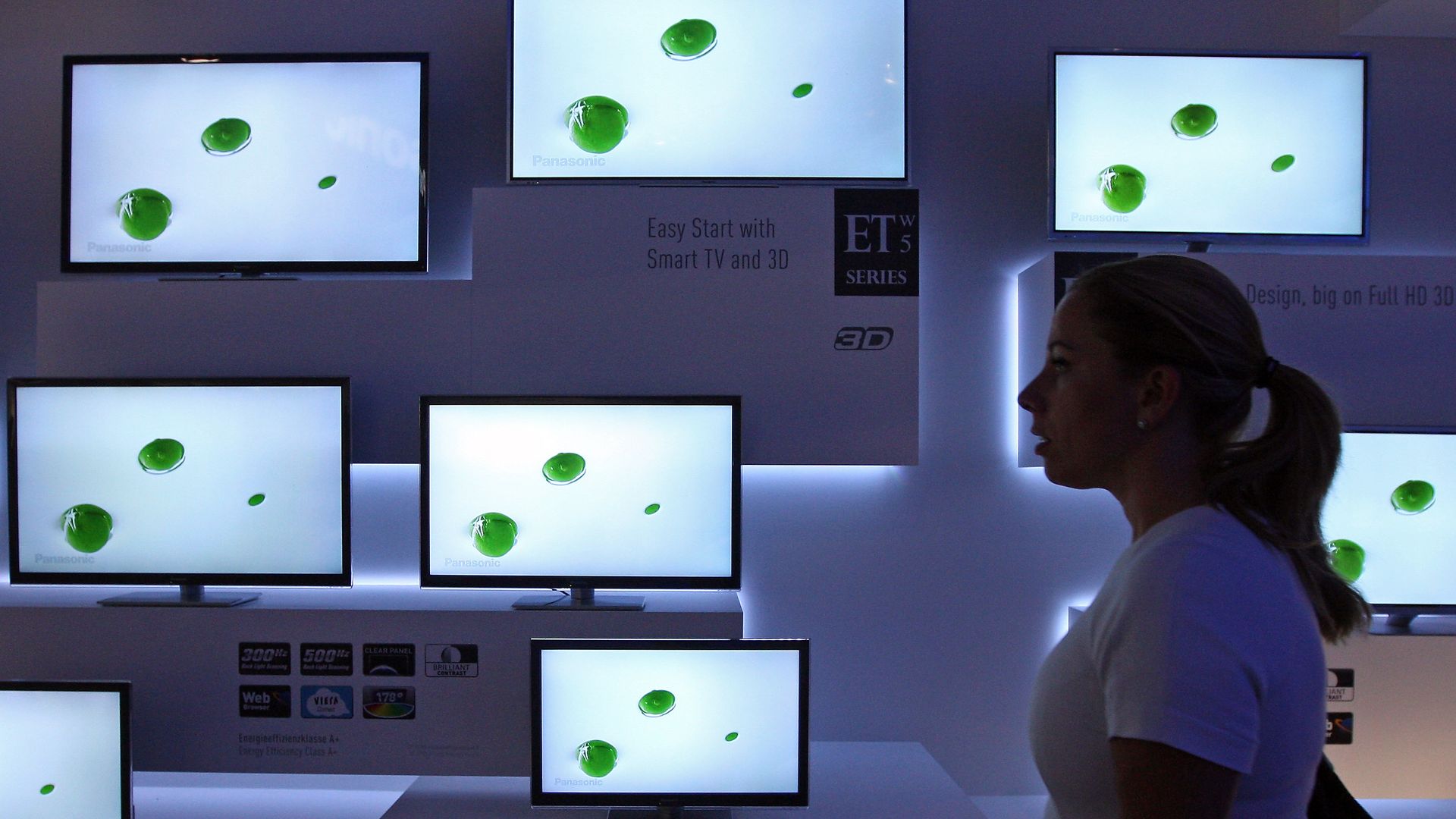 A woman walking by Smart TVs