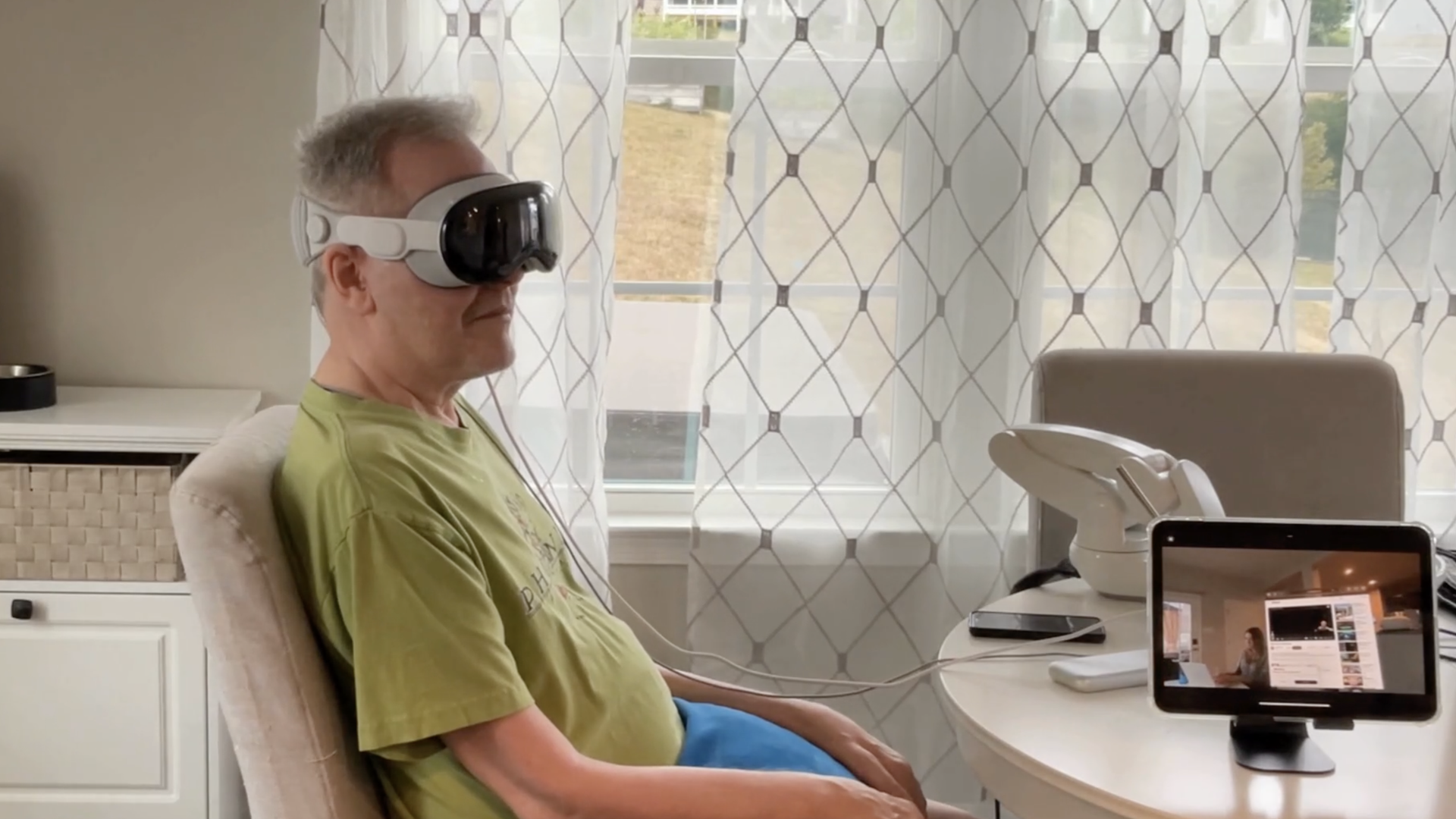 man wearing a green shirt sitting in a chair wearing an Apple Vision Pro headset 