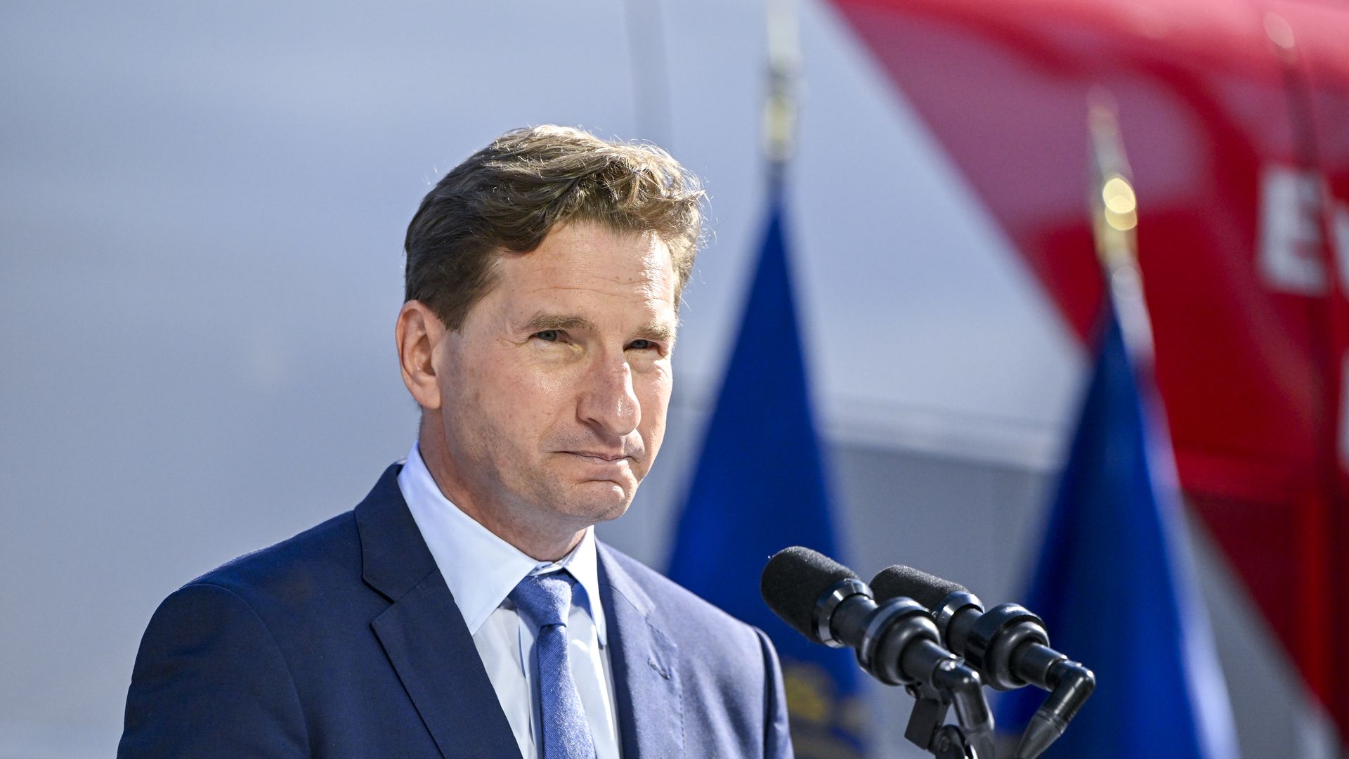 Dean Philips at a microphone in a blue suit and tie