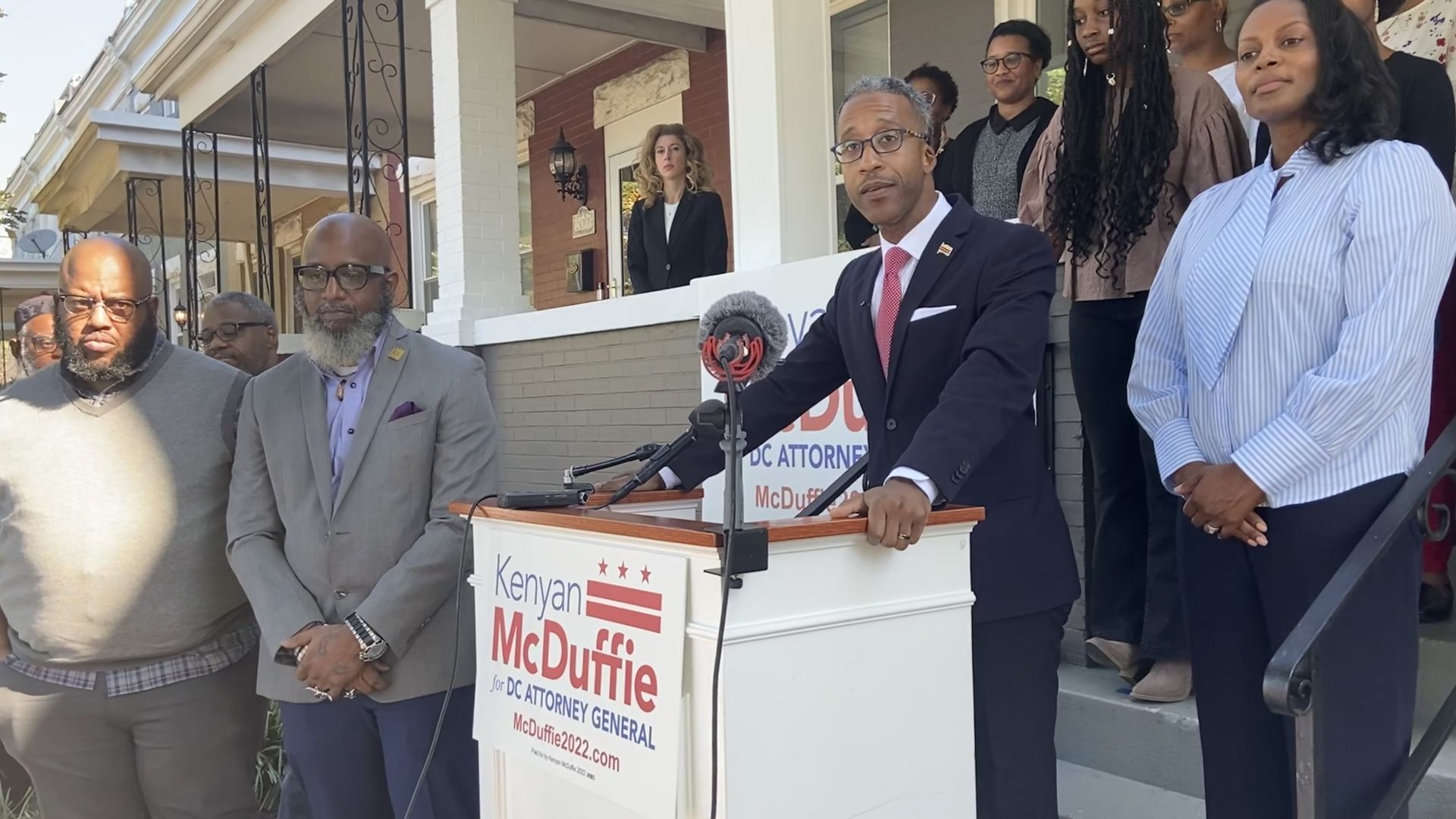 Council member Kenyan McDuffie speaks before a podium surrounded by family and friends.